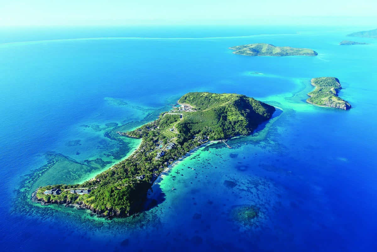 斐濟群島驚嘆的空中景觀 壁紙 — 俯瞰一個鬱鬱蔥蔥的綠色島嶼，周圍環繞著充滿活力的藍綠色和深藍色海水，近岸可見珊瑚礁。