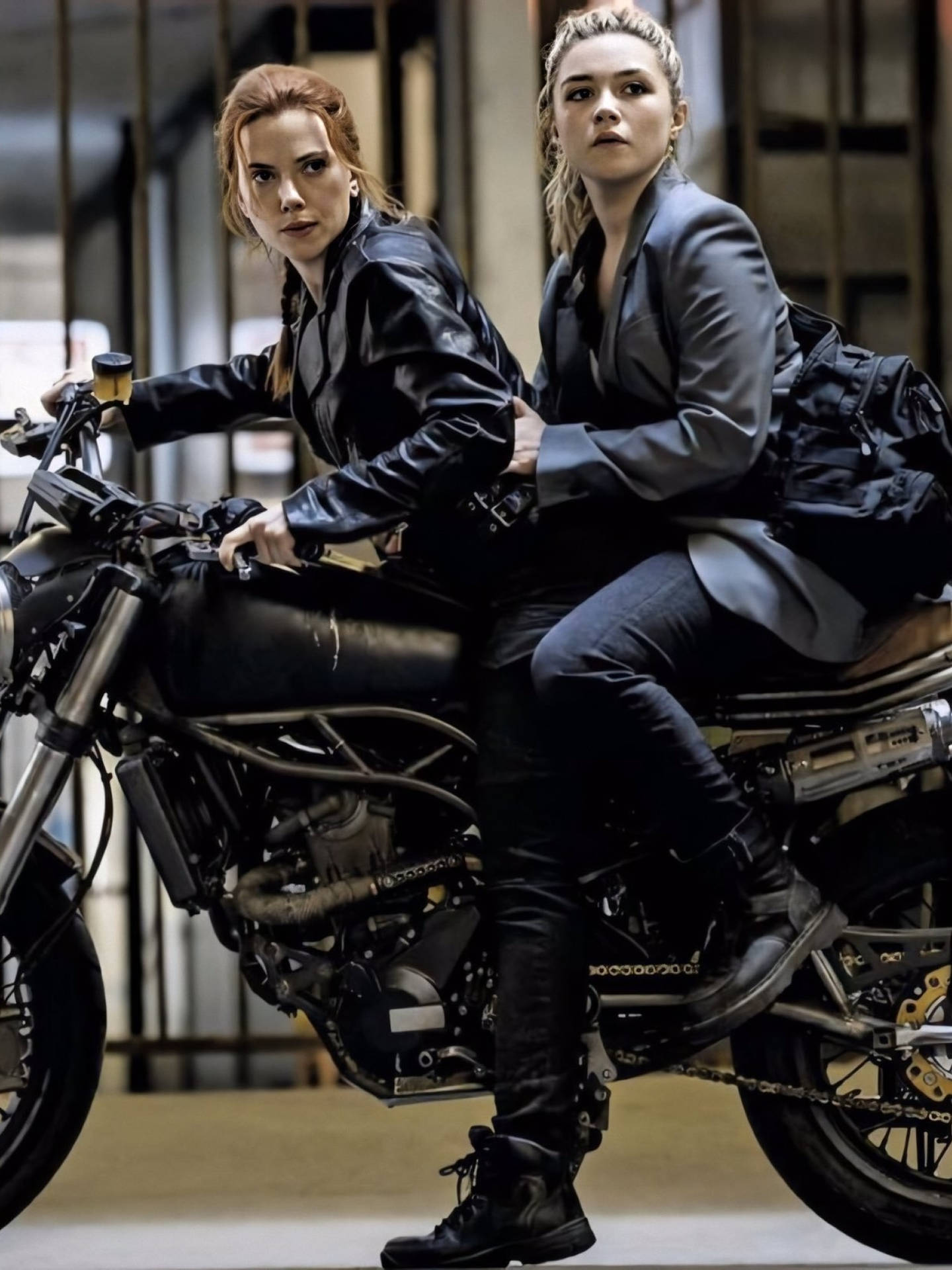 兩位身穿黑色皮革和西裝的女性在工業環境中騎摩托車。