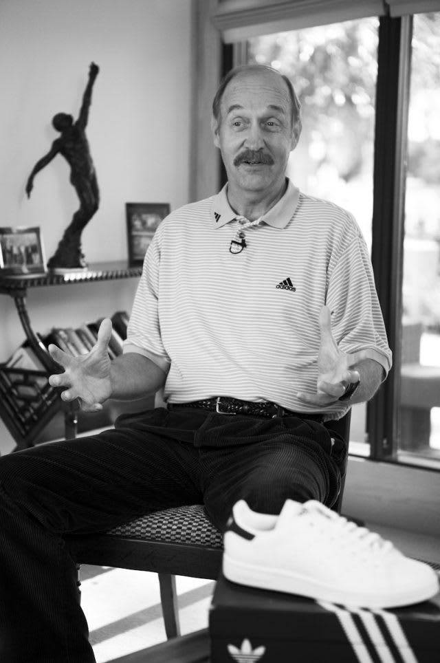 留鬍鬚的男人坐在白色 adidas 運動鞋旁邊做手勢。