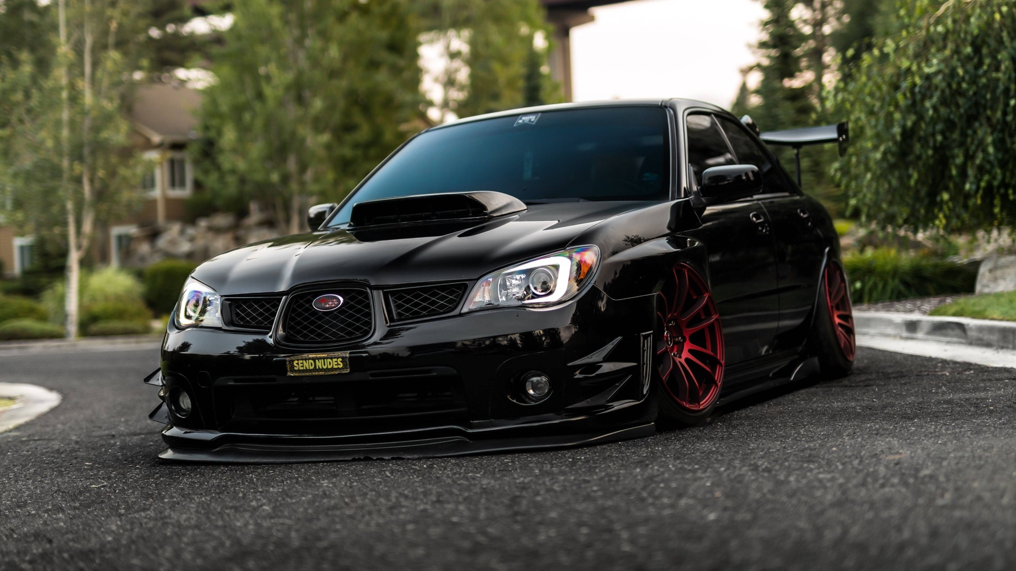 斯巴魯Impreza Jet Black 壁紙 — 一架亮黑色Subaru WRX STI配紅色輪圈，停泊在瀝青路上，周圍有綠樹和房屋。