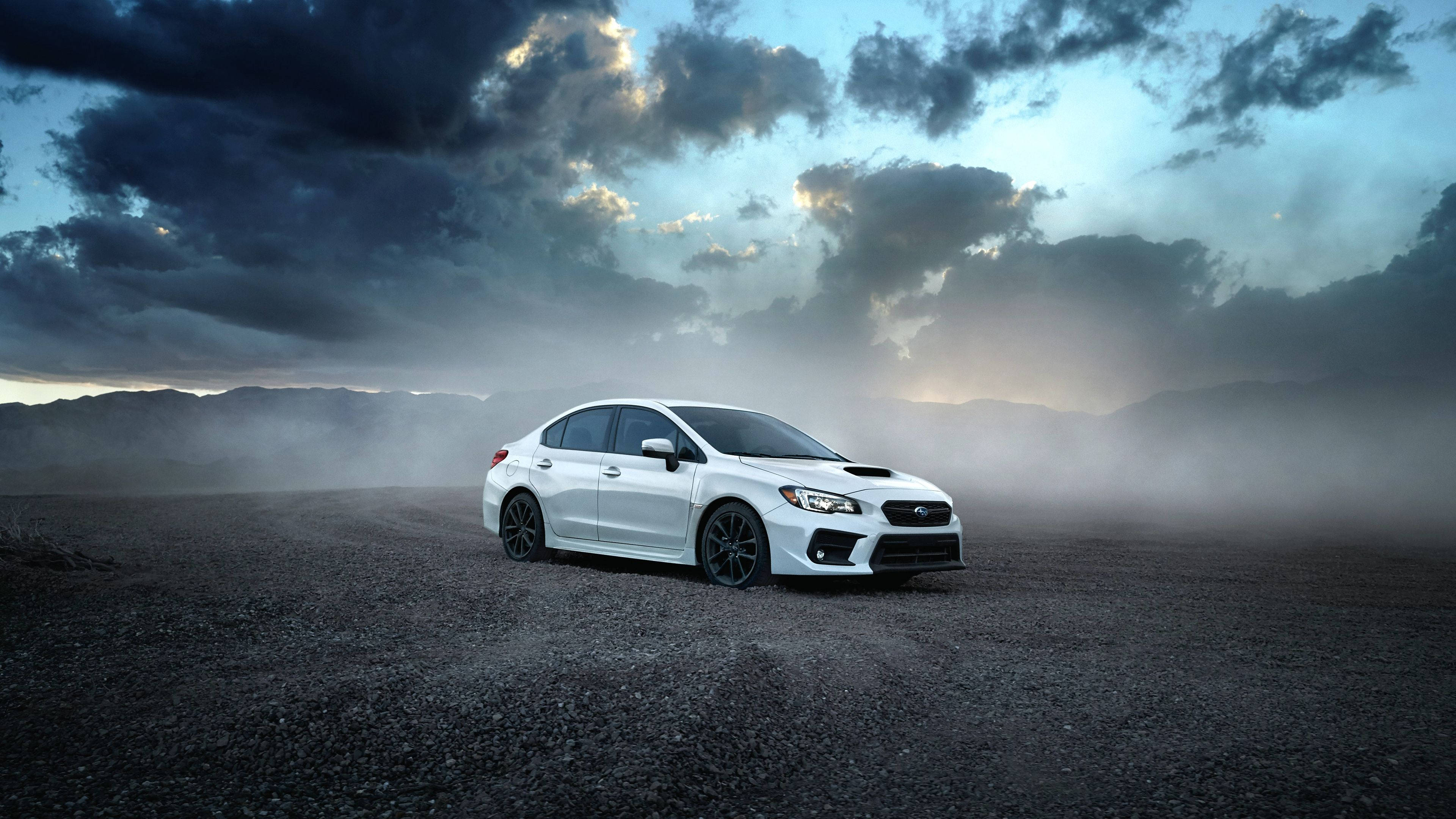 斯巴魯停泊於黑砂地 壁紙 — 一架白色Subaru WRX STI獨自佇立在碎石平原上，天空佈滿暴風雲和霧氣，呈現戲劇性的暮色。