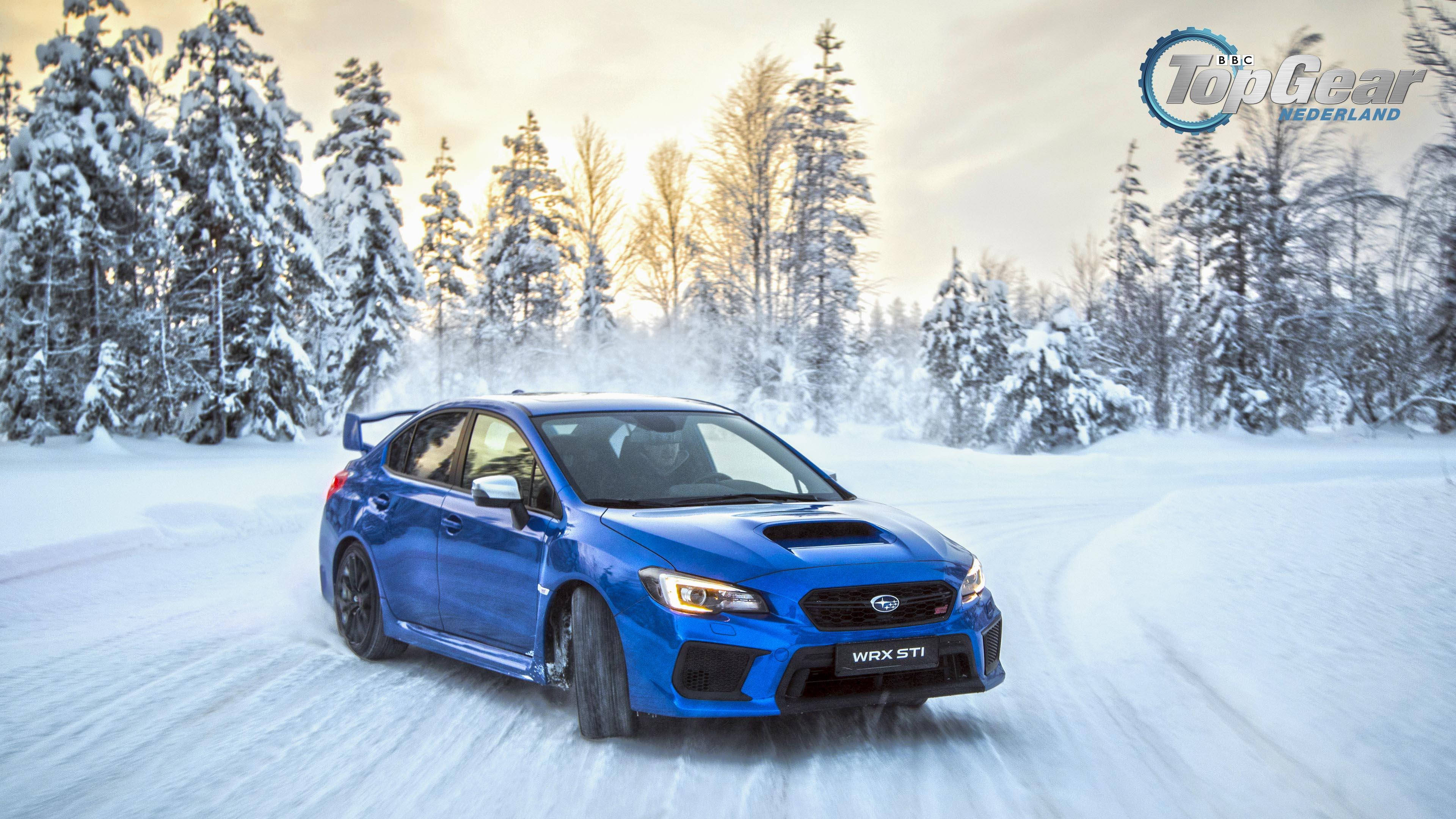 斯巴魯雪地漂移 壁紙 — 一輛充滿活力的藍色 Subaru WRX STI 在雪地森林中疾馳，輪胎濺起雪花，天空呈現柔和的金色。