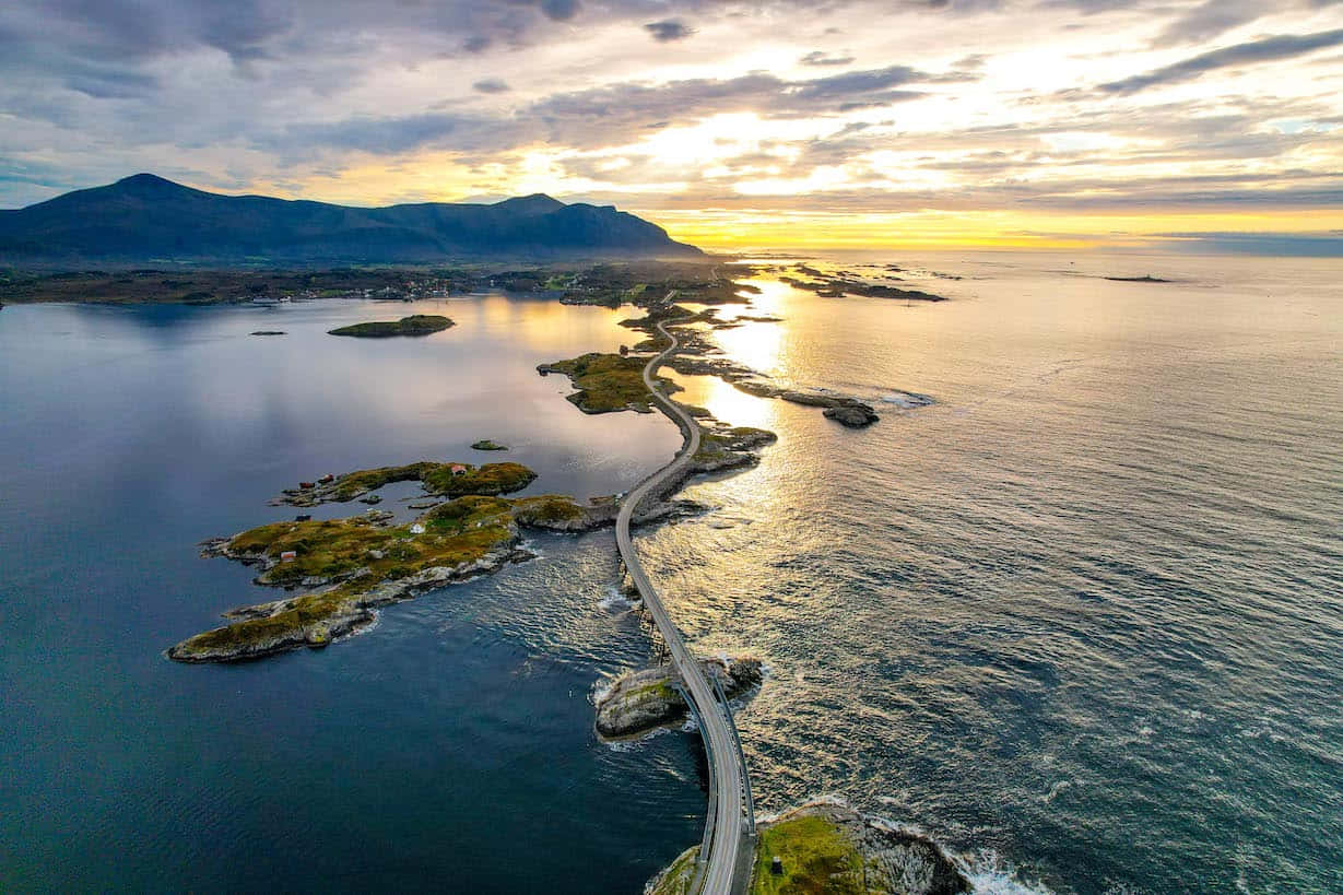 日落時分一條蜿蜒的海岸公路，海面和遠處山脈上反射著金色光芒。