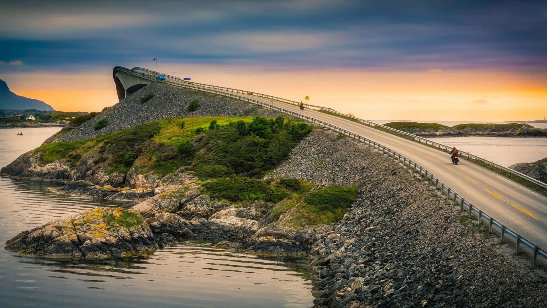 電單車手在日落時分騎行在一條蜿蜒的海岸公路上，穿過岩石島嶼。
