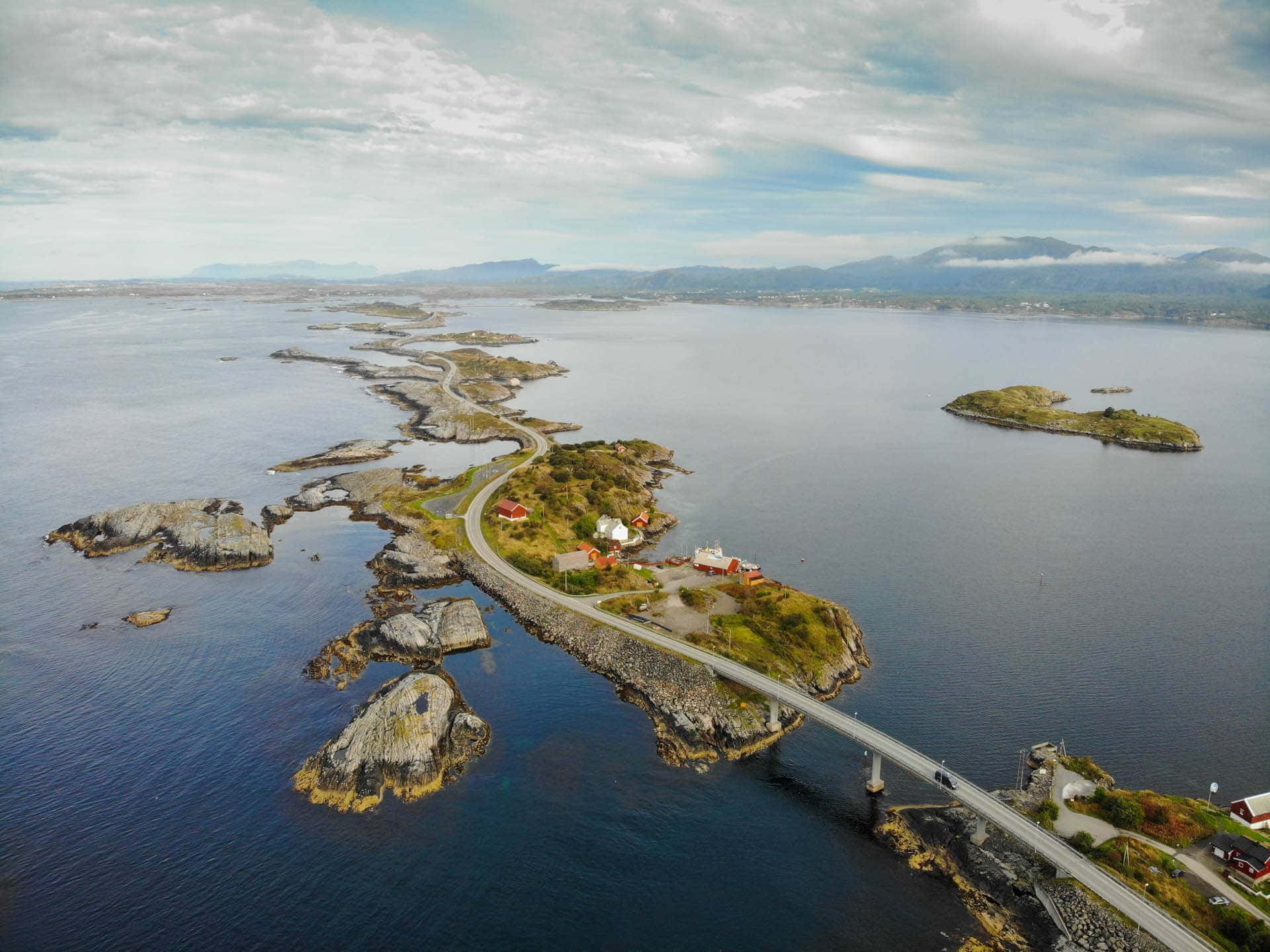 海岸道路蜿蜒於岩石島嶼之間，有紅頂房屋和藍色海水。