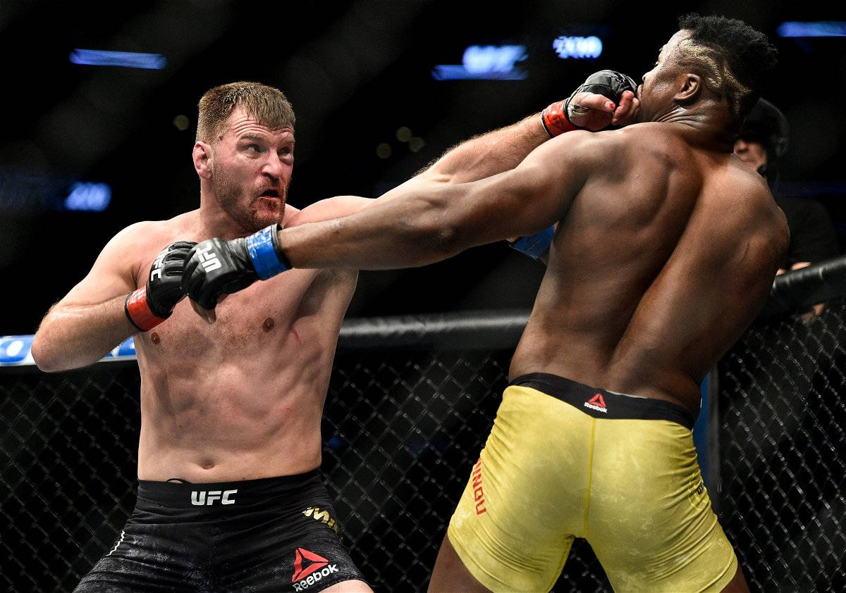 斯泰普·米奧奇交換左勾拳 壁紙 — 兩名MMA拳手在激烈的鐵籠賽中交鋒，其中一人在明亮的場館燈光下向對方臉部揮出強力一拳。