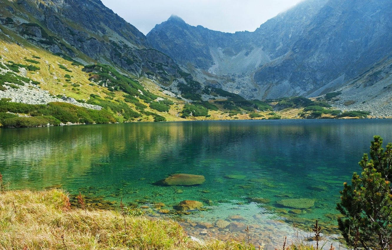 斯洛伐克山與湖泊 壁紙 — 一個寧靜的高山湖泊，清澈見底的碧藍湖水，坐落於崎嶇岩石山脈之間，天空柔和。