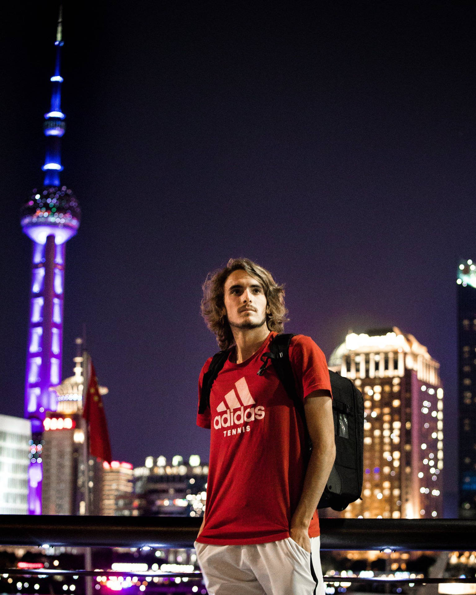 身穿紅色網球衫的年輕男子夜晚站在上海城市燈光前。