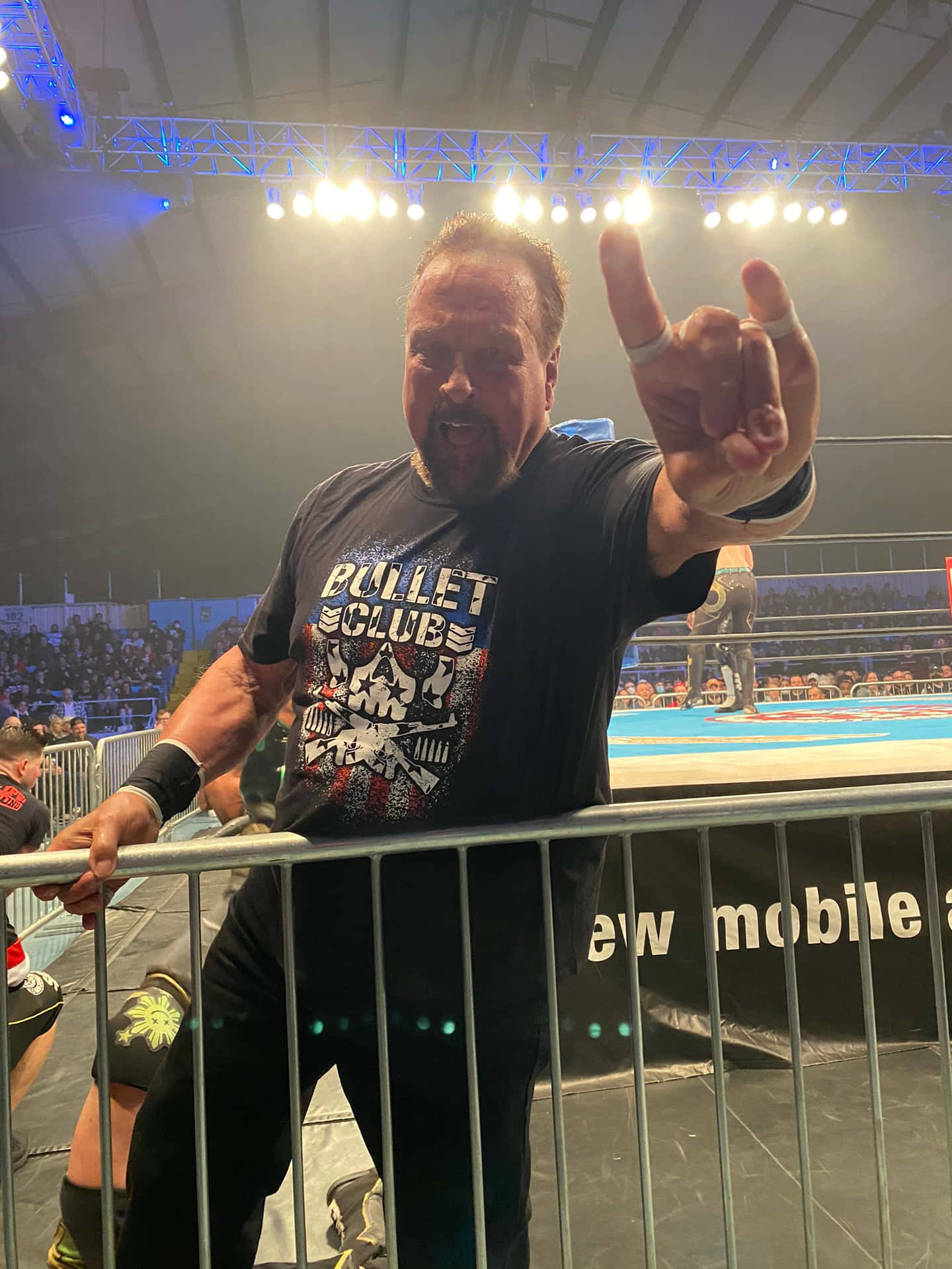 穿著 Bullet Club 襯衫的摔角手在金屬護欄後面向人群做出搖滾手勢。