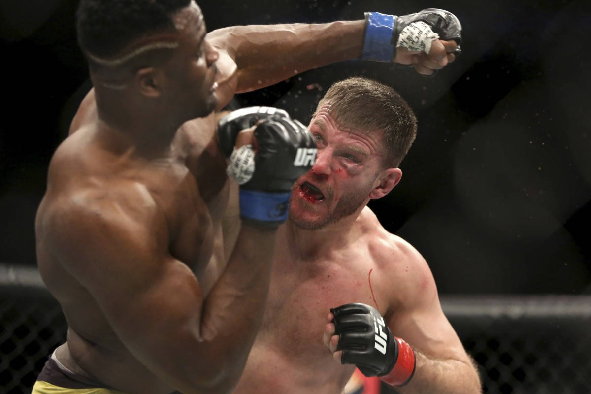 斯蒂普·米奧奇躲避左勾拳 壁紙 — 一名拳手在UFC八角籠中對對手使出殘酷一拳，鮮血飛濺，表情激烈。