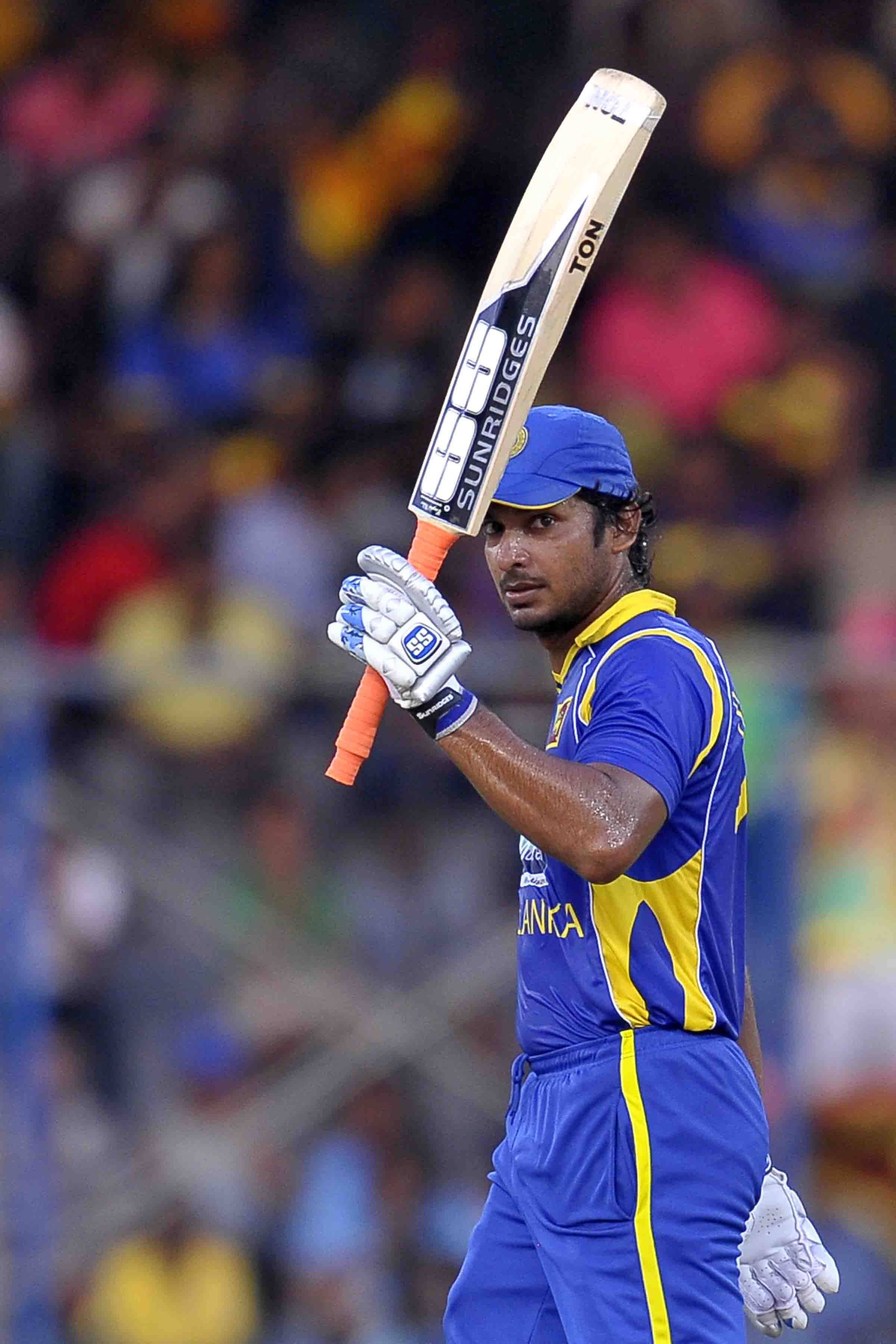 斯里蘭卡板球運動員Kumar Sangakkara 壁紙 — 一名身穿藍黃色球衣的斯里蘭卡板球手在夜間比賽中，在球場燈光下高舉球棒慶祝勝利。