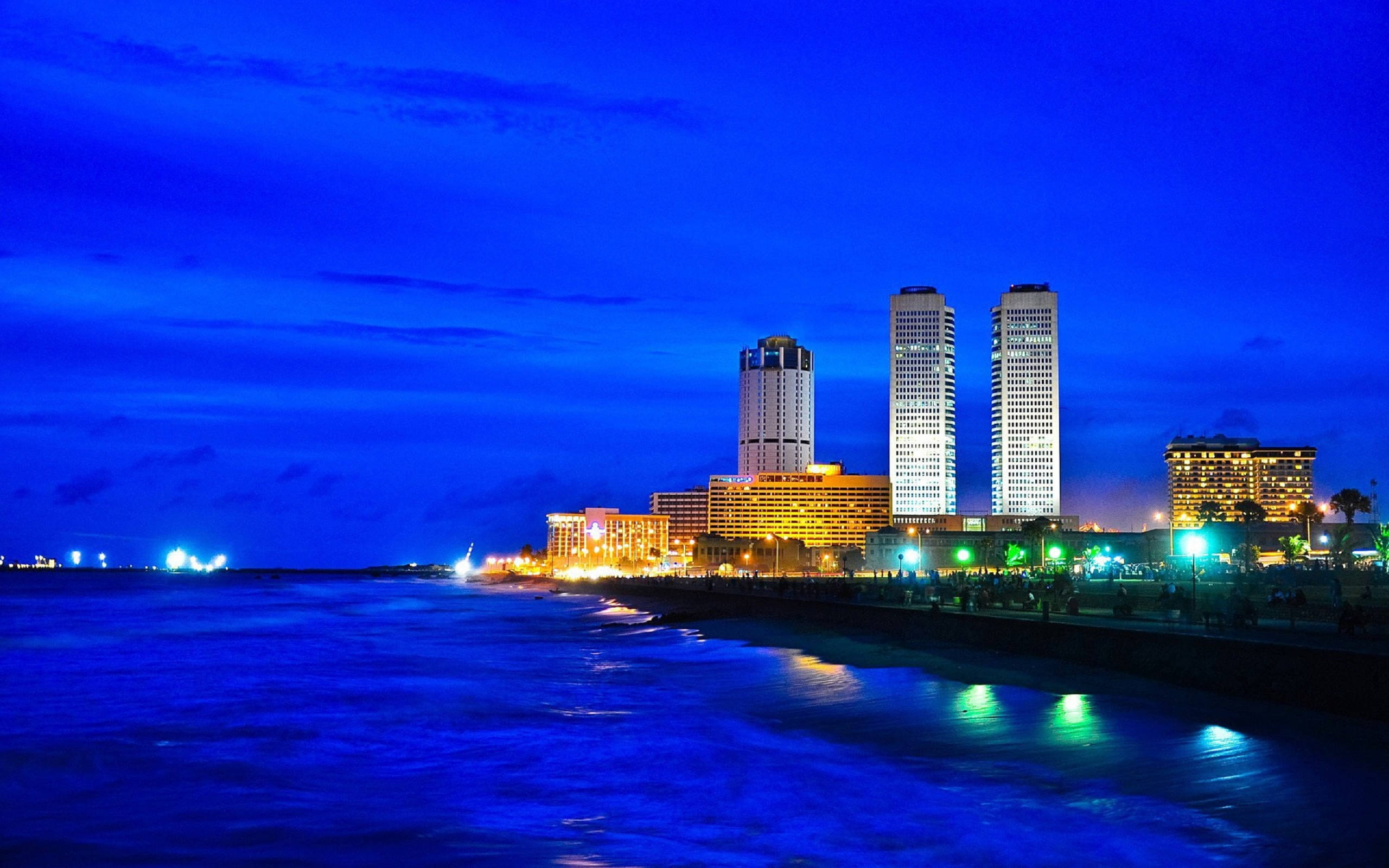 斯里蘭卡科倫坡WTCC夜景天際線 壁紙 — 黃昏時分充滿活力的海岸城市景觀，閃爍的摩天大樓倒映在深藍色的海浪上。