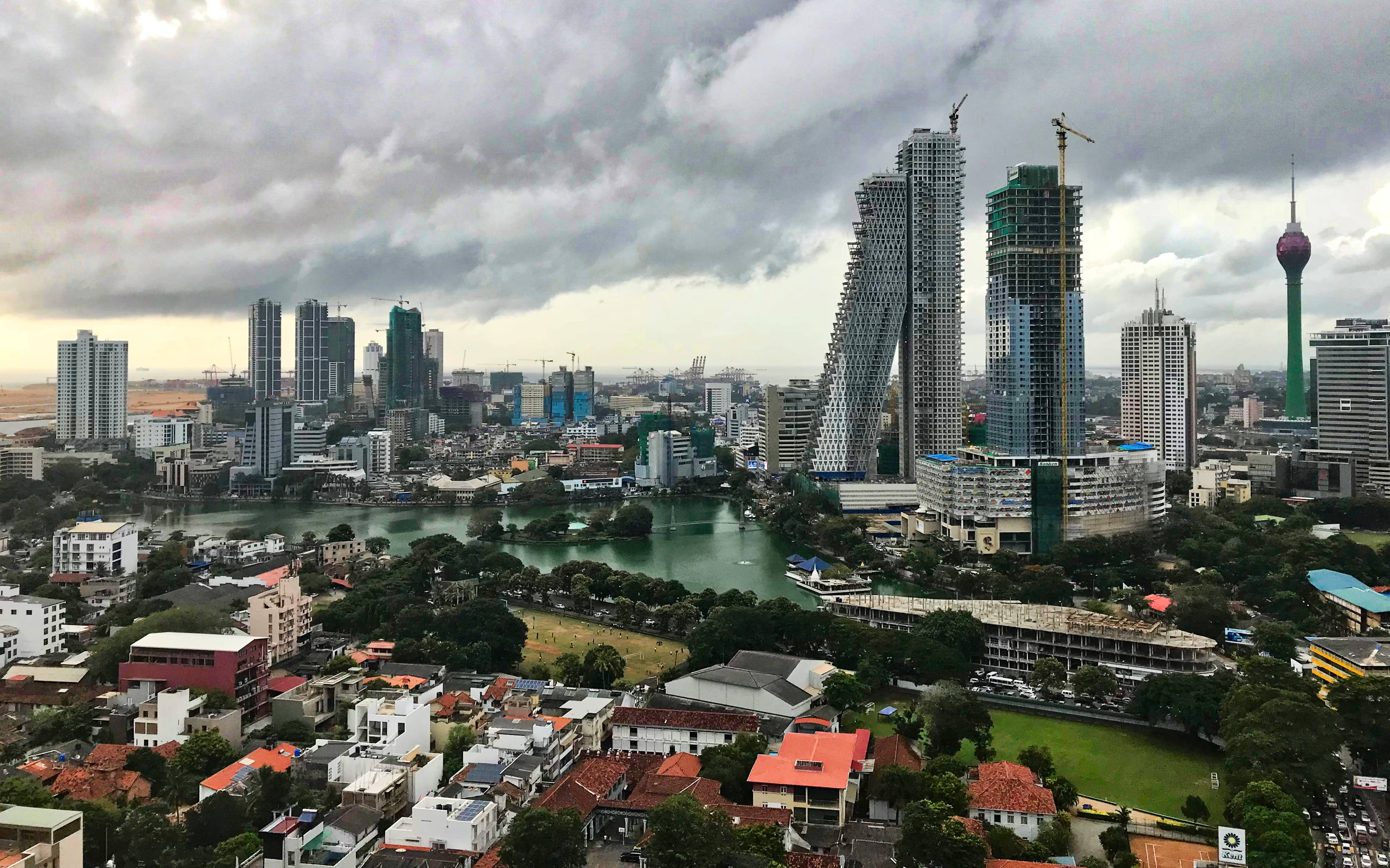 斯里蘭卡科倫坡城市景觀 壁紙 — 在暴風雲下戲劇性的城市天際線，河流蜿蜒穿過密集的住宅區和現代高層建築。
