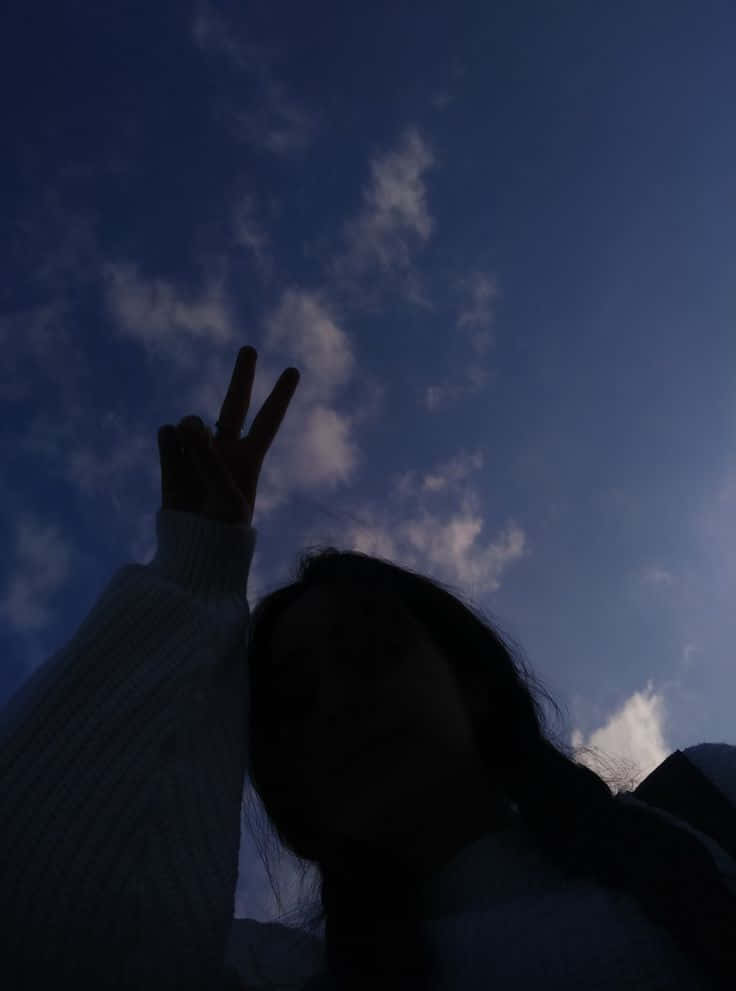 剪影人物在暮色天空下做出和平手勢