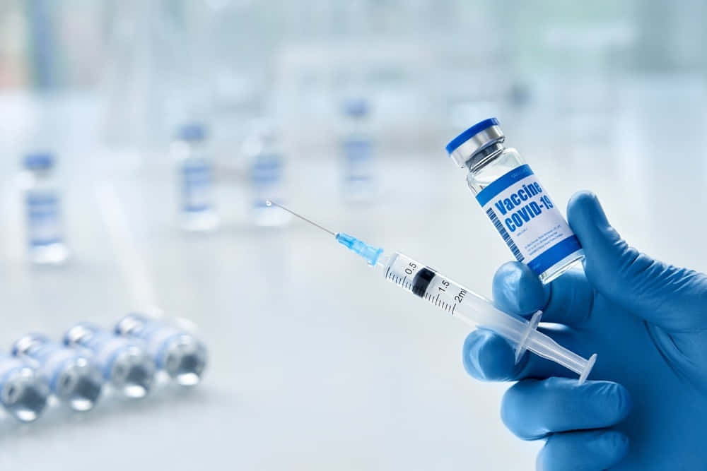 戴藍色手套的手在實驗室中拿著注射器和COVID-19疫苗藥瓶。