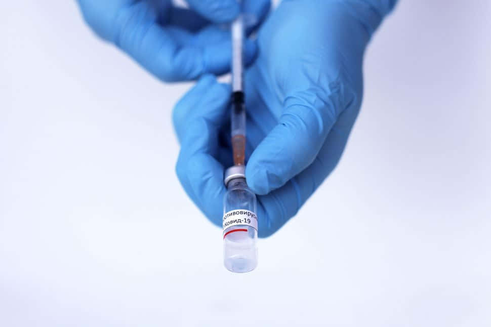 戴藍色手套的手用注射器從藥瓶中抽取疫苗。