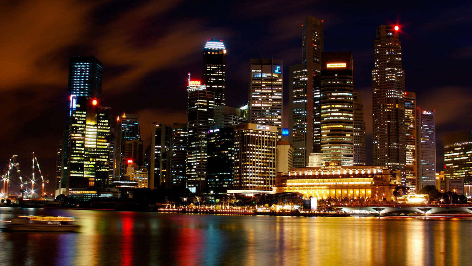 新加坡城市夜景 壁紙 — 令人目眩的夜景城市景觀，高聳的摩天大樓在平靜的河面上反射出鮮豔的燈光，船隻穿梭而過。