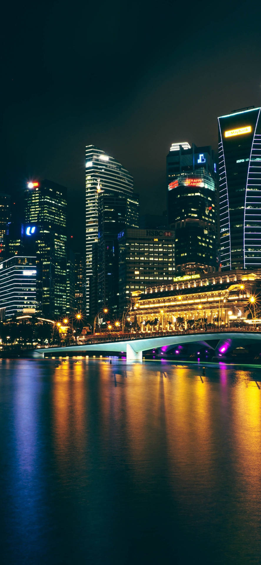 現代城市天際線的夜景，有明亮的建築物和水上的橋樑。