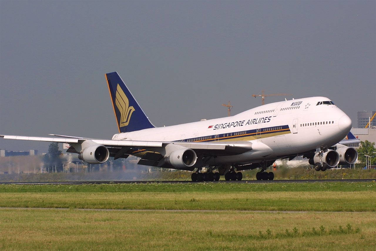 新加坡航空波音747在跑道上，背景有草地和機場建築。