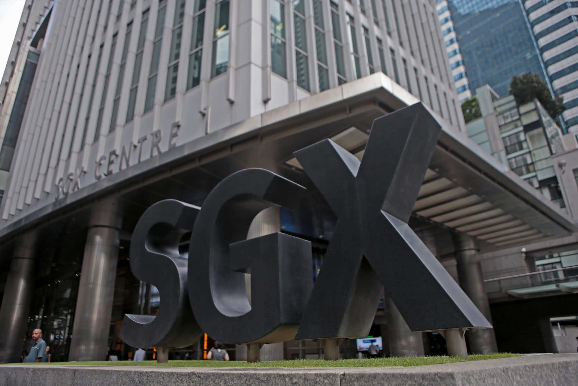 SGX標誌雕塑矗立在現代商業大樓前，有行人經過。