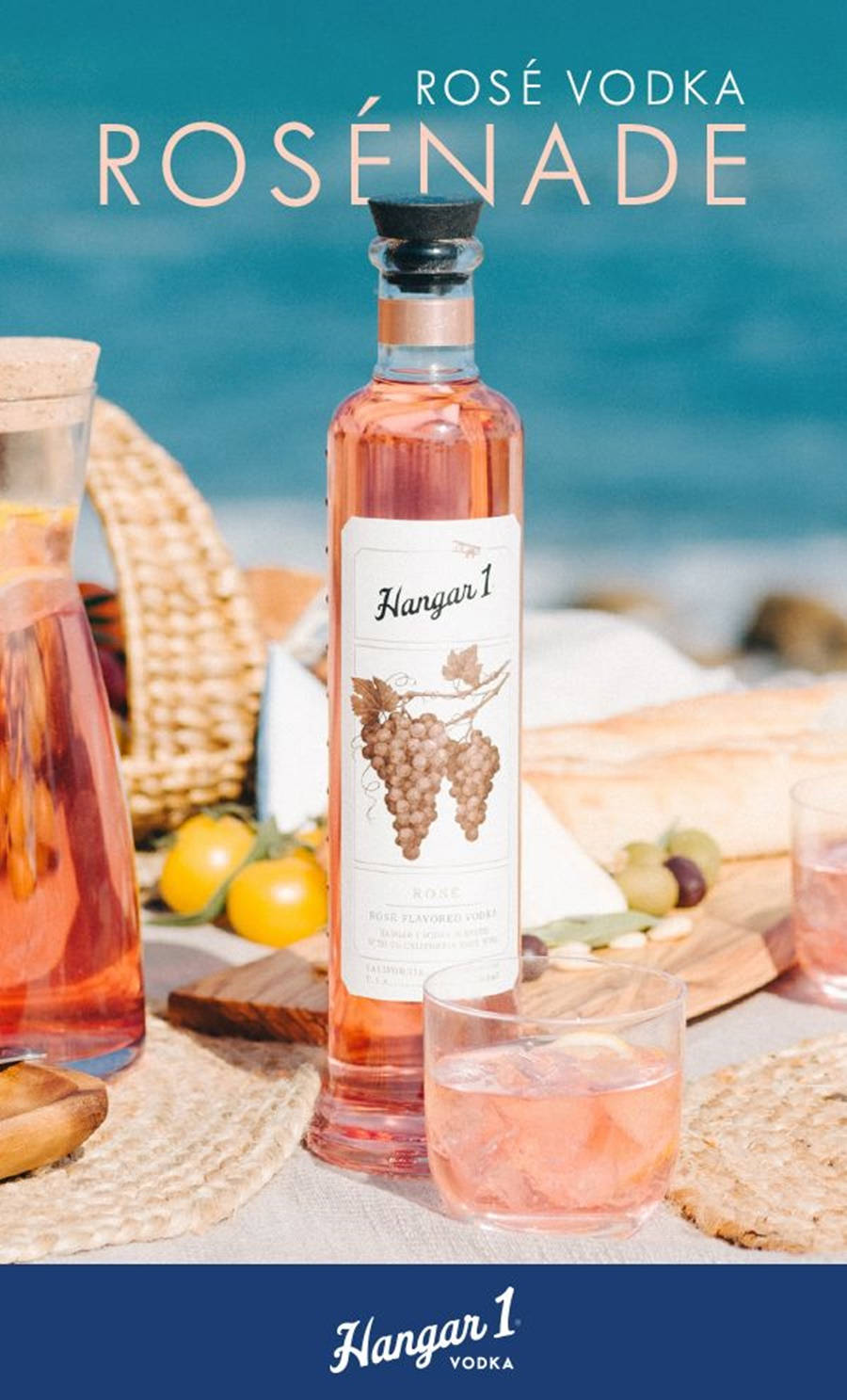 新口味Hangar 1水果系列 壁紙 — 一瓶Hangar 1 Rosé Vodka放在沙灘毛巾上，旁邊有一杯雞尾酒和新鮮水果，在明亮的陽光下。