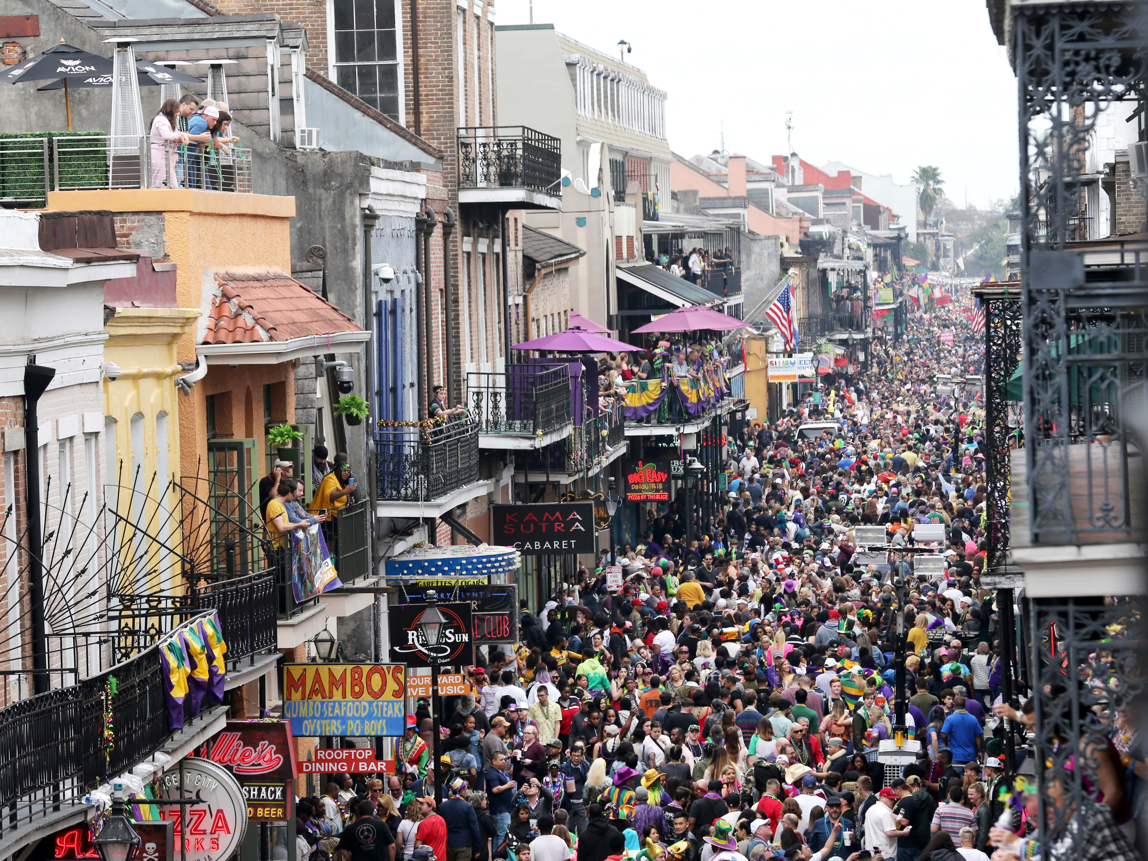 Mardi Gras 桌布 壁紙 — 新奧爾良一條熙熙攘攘的街道，擠滿了在色彩繽紛的陽台和節日旗幟下慶祝的人群。