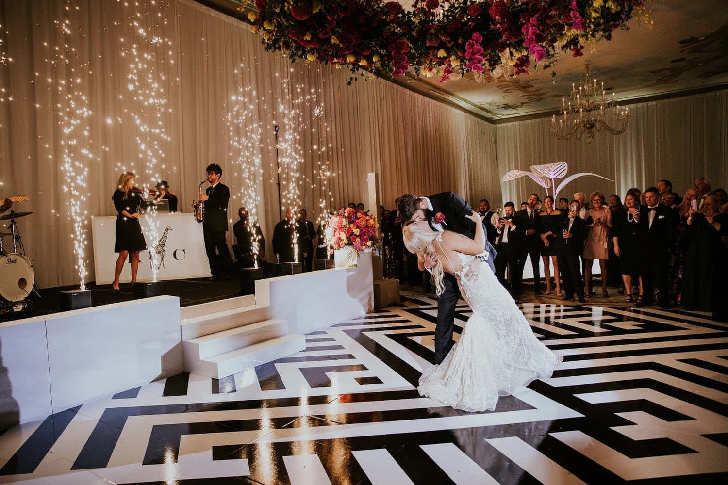 Black And White Wedding 桌布 壁紙 — 新娘和新郎在黑白幾何圖案的舞池上熱情接吻，賓客觀看，煙花從窗簾背景中如瀑布般落下。