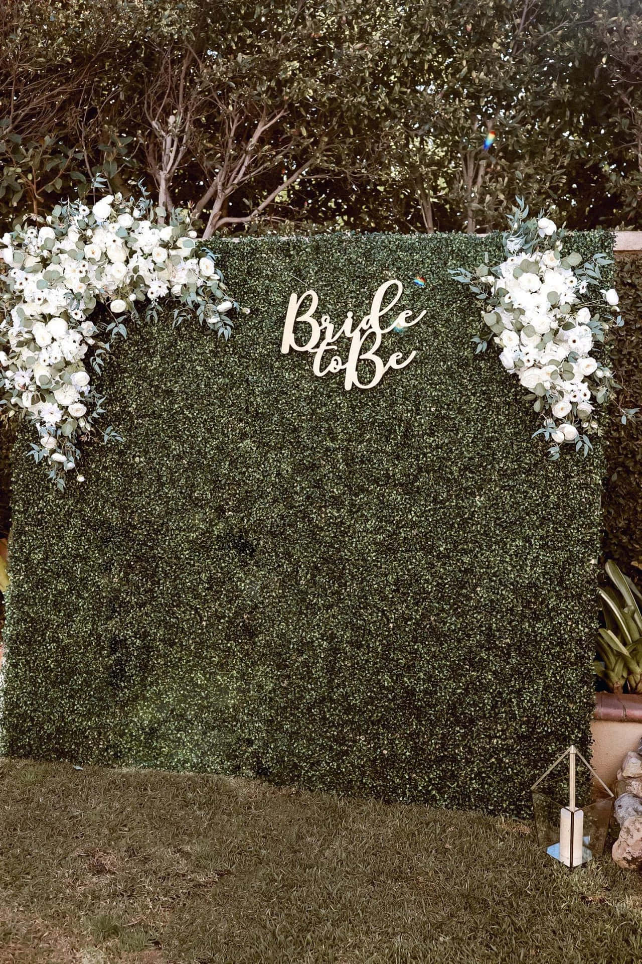 綠色樹籬牆，飾有白色花朵和 bride to be 標誌。