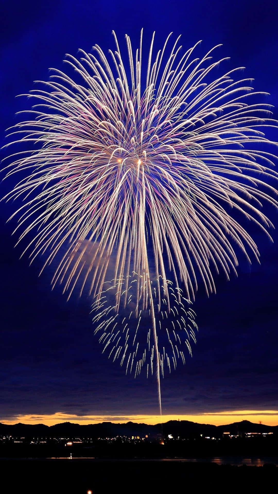 煙火在夜空中山脈和城市燈光上方爆炸。