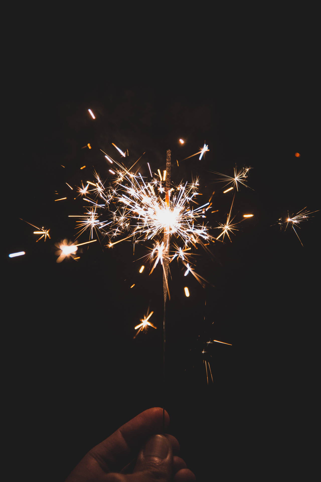 手拿著點燃的煙花棒，在黑暗背景下發出明亮的金色火花。 — 新年動畫 壁紙