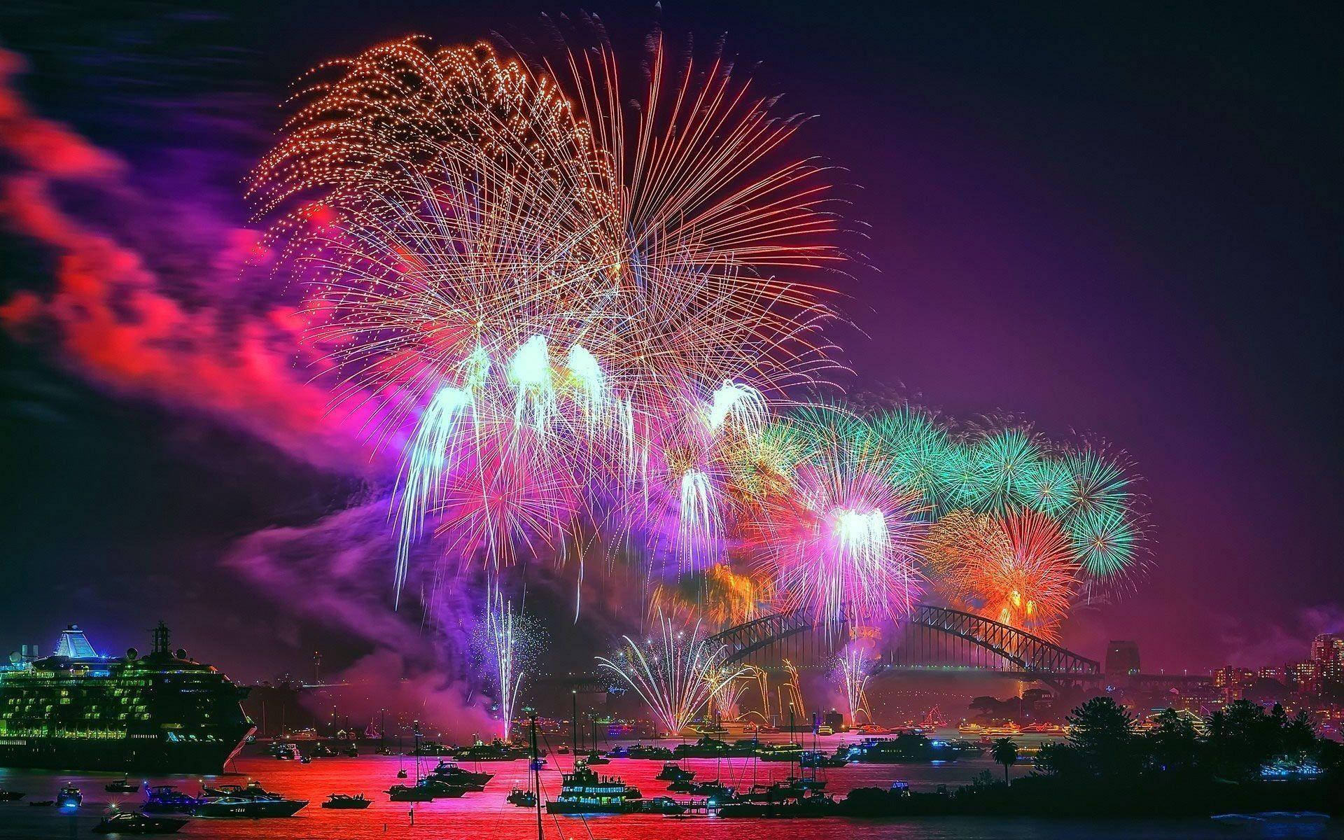 新年夜煙火 壁紙 — 色彩繽紛的煙火在夜間於悉尼港上空綻放，以耀眼色彩照亮標誌性大橋及水面。