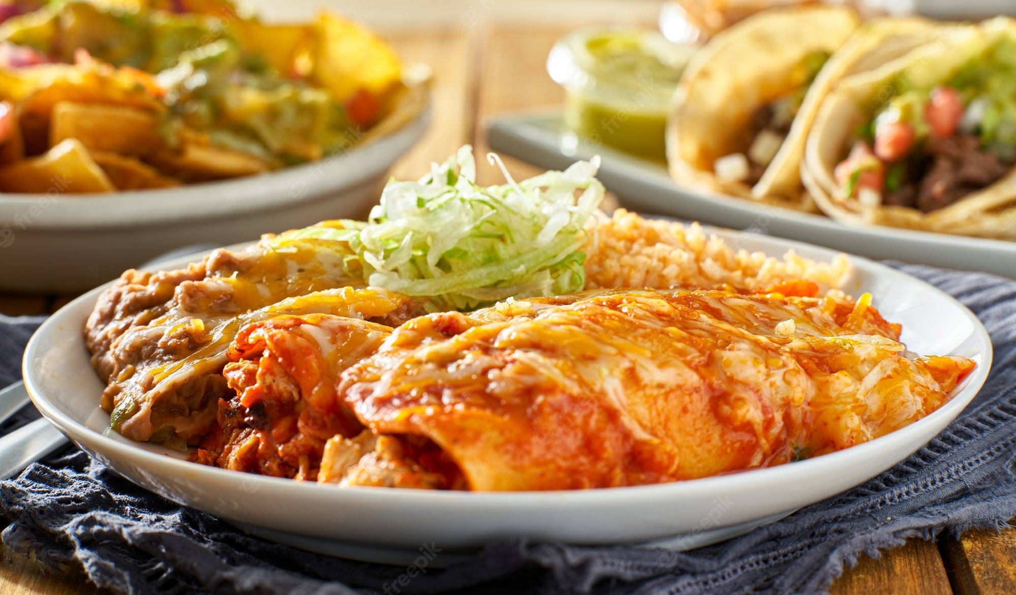 新煮 enchiladas 盤中盛放 壁紙 — 金黃色的玉米卷餅浸在紅醬和融化芝士中，放在白色碟子上，伴以新鮮生菜裝飾。