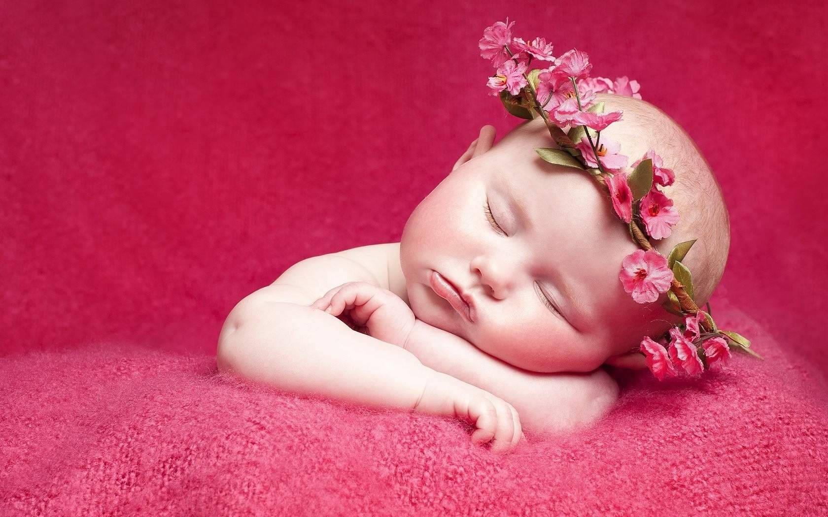 一個睡著的新生嬰兒，戴著粉紅色花冠，躺在粉紅色毯子上。