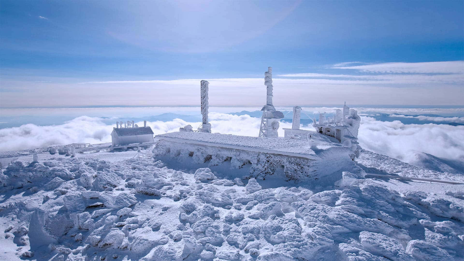 新罕布什爾州白山天文台冬季景觀 壁紙 — 一個被雪覆蓋的山間車站，坐落在雲海之上，天空清澈湛藍。