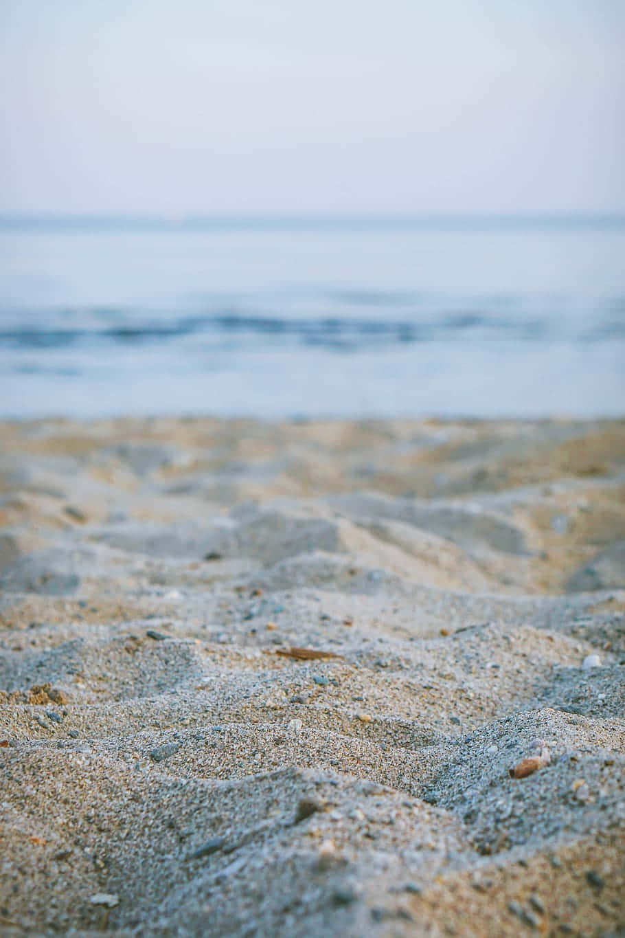 沙灘上柔軟嘅沙粒，背景係溫柔嘅海浪