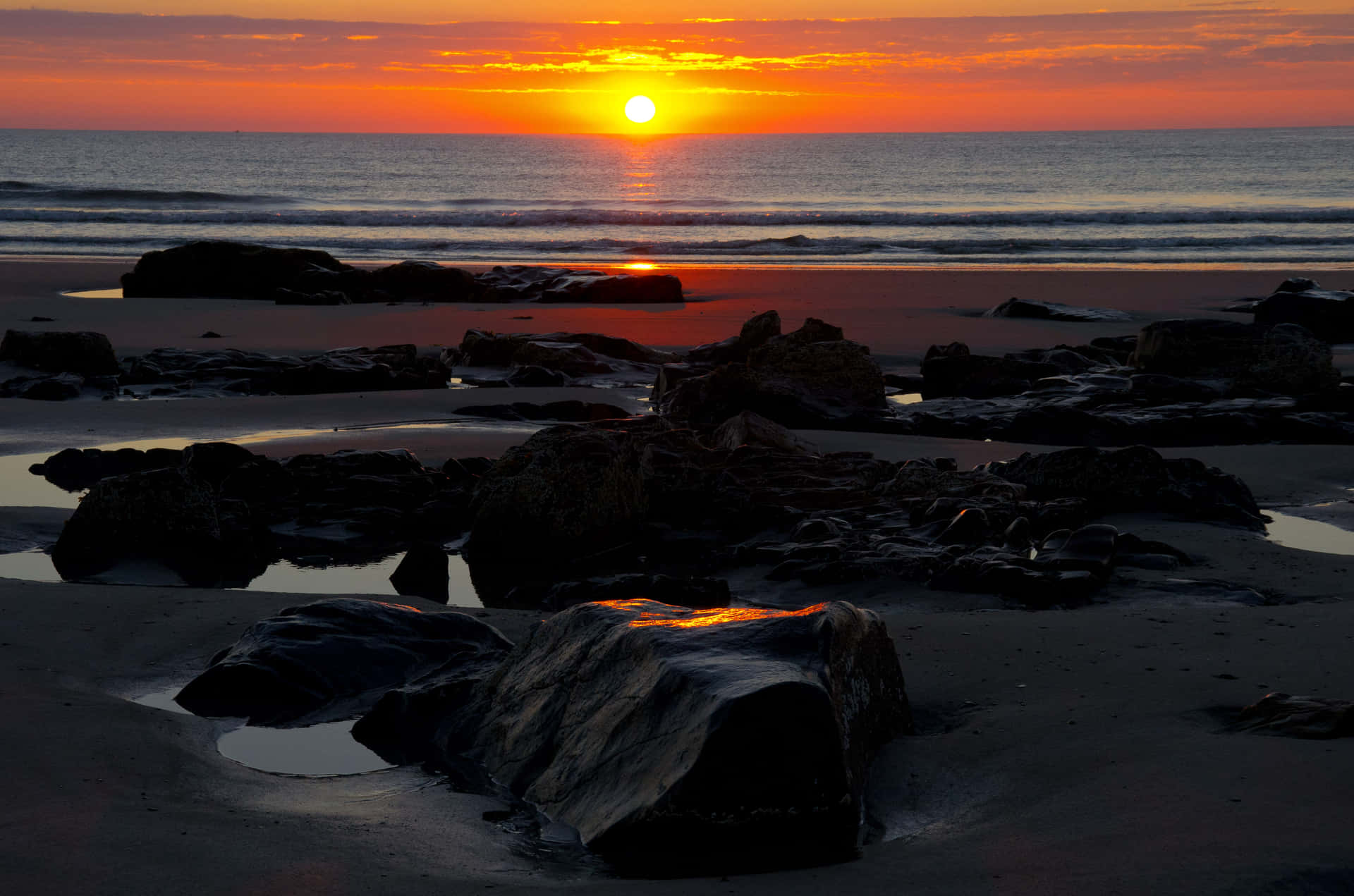 海洋上的夕陽，海灘上的岩石反射溫暖的色彩