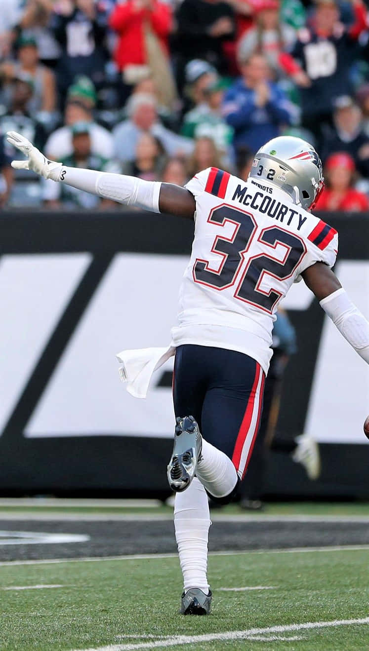 Devin Mccourty 桌布 壁紙 — 新英格蘭愛國者隊球員麥考蒂身穿白色32號球衣，在陽光明媚的足球場上張開雙臂慶祝比賽。
