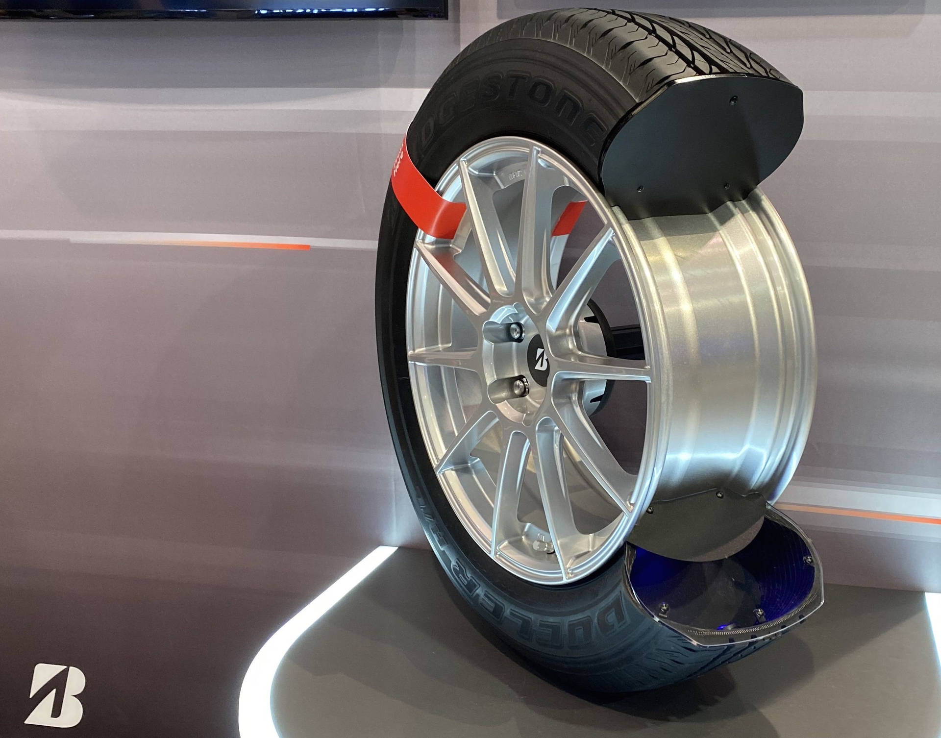 一個安裝在銀色合金輪圈上的Bridgestone輪胎，在現代照明展示架上展示。
