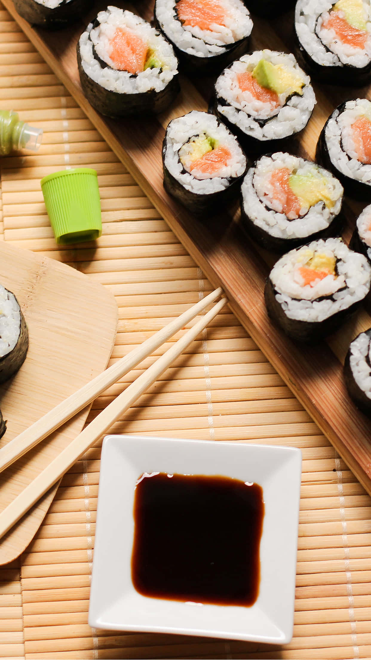 Sushi 桌布 壁紙 — 新鮮三文魚牛油果壽司卷擺放在木托盤上，旁邊有醬油和筷子在竹蓆上。