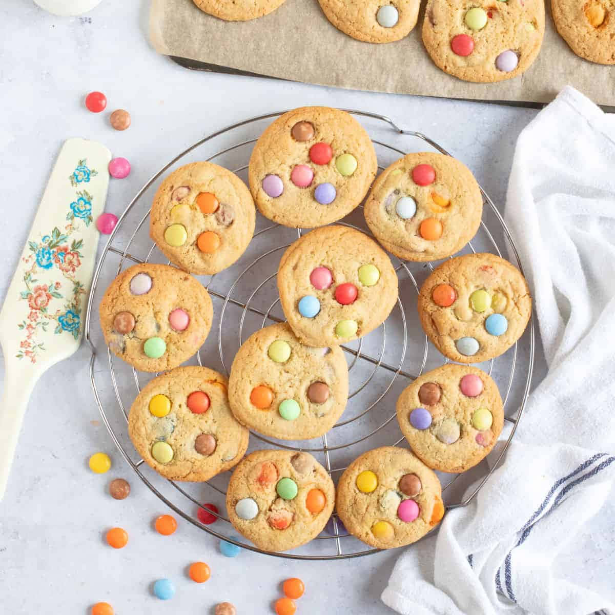 Cookie 桌布 壁紙 — 新鮮出爐的彩色M&M曲奇在金屬架上冷卻，旁邊有花卉圖案刮刀和白色毛巾。