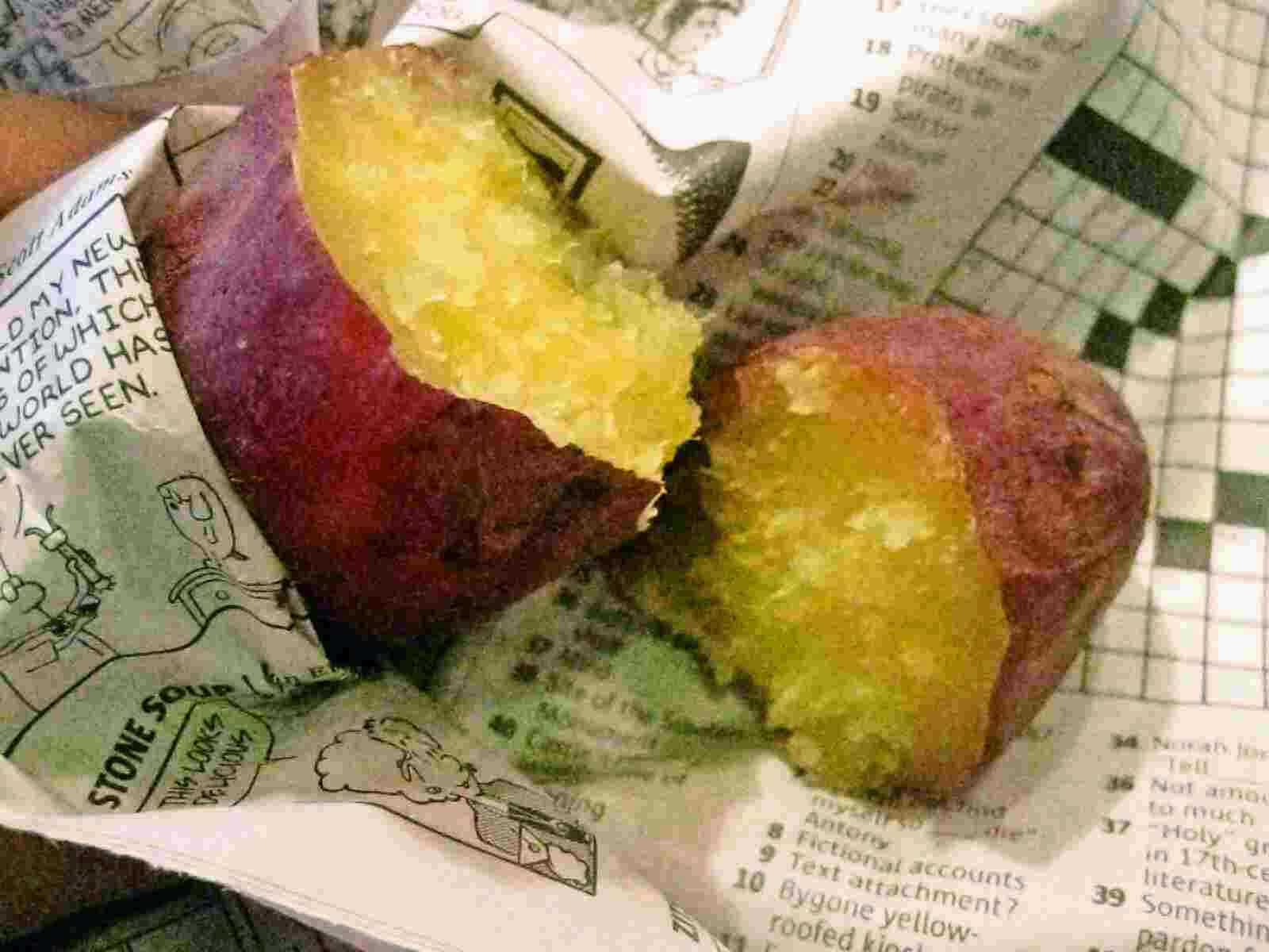 Yellow Sweet Potato 桌布 壁紙 — 新鮮出爐的番薯切開，露出柔軟的金黃色果肉，放在有填字遊戲的報紙上。