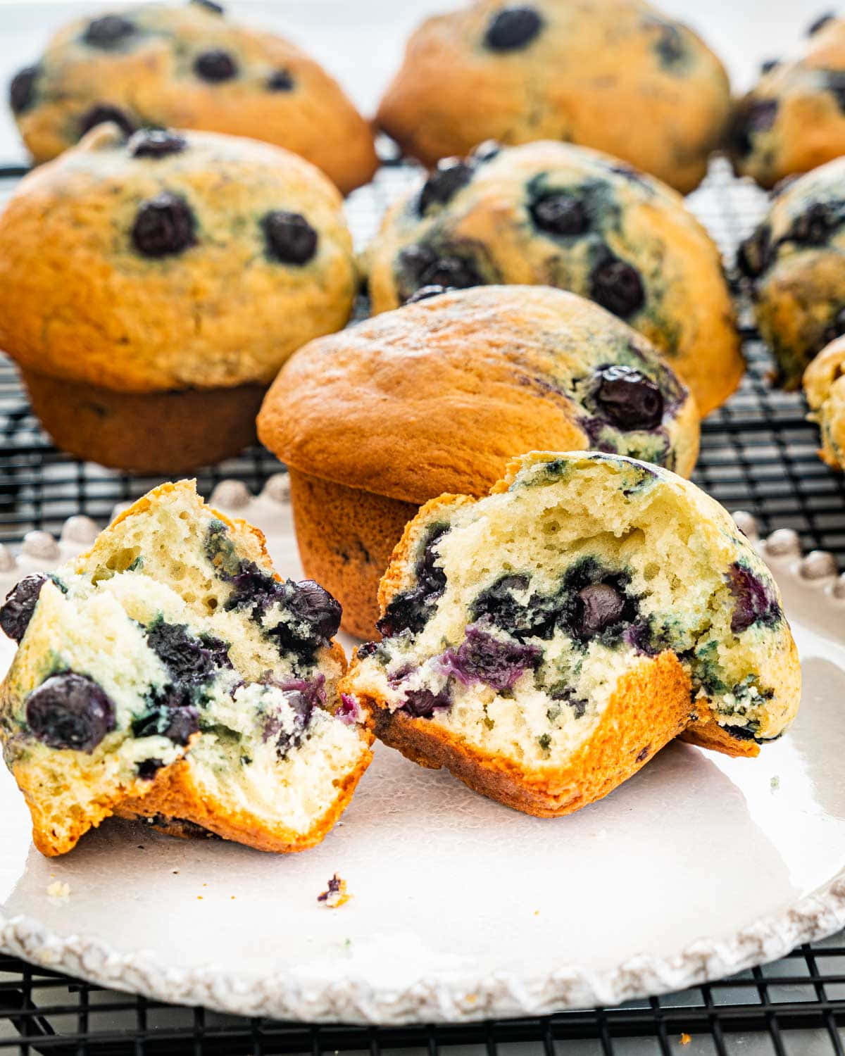 Blueberry Muffins 桌布 壁紙 — 新鮮出爐的藍莓鬆餅，金黃外皮和多汁莓果放在冷卻架和碟子上。