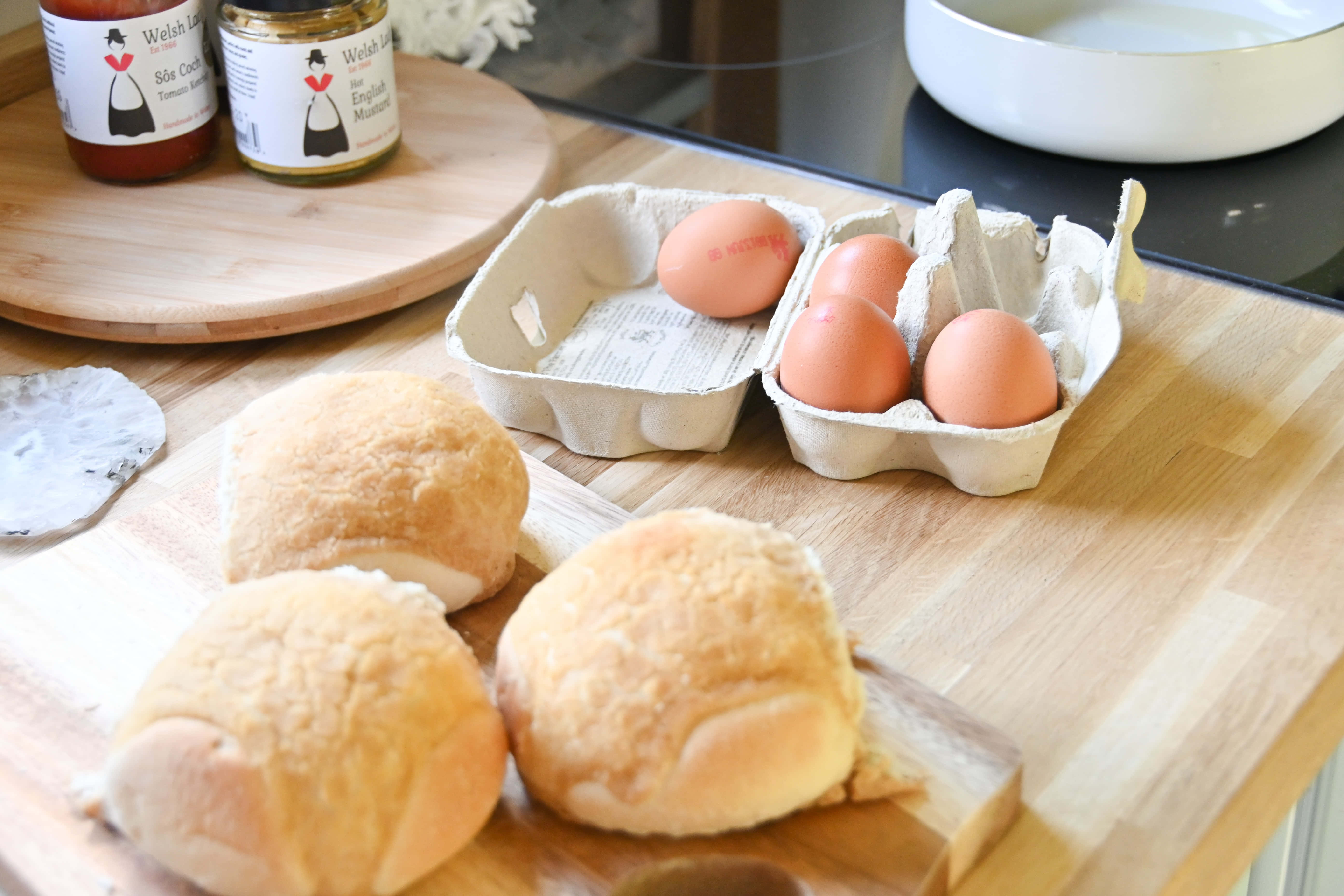 Brown Eggs 桌布 壁紙 — 新鮮出爐的金黃色麵包卷和棕色雞蛋放在木製枱面上，旁邊是威爾斯調味醬罐。