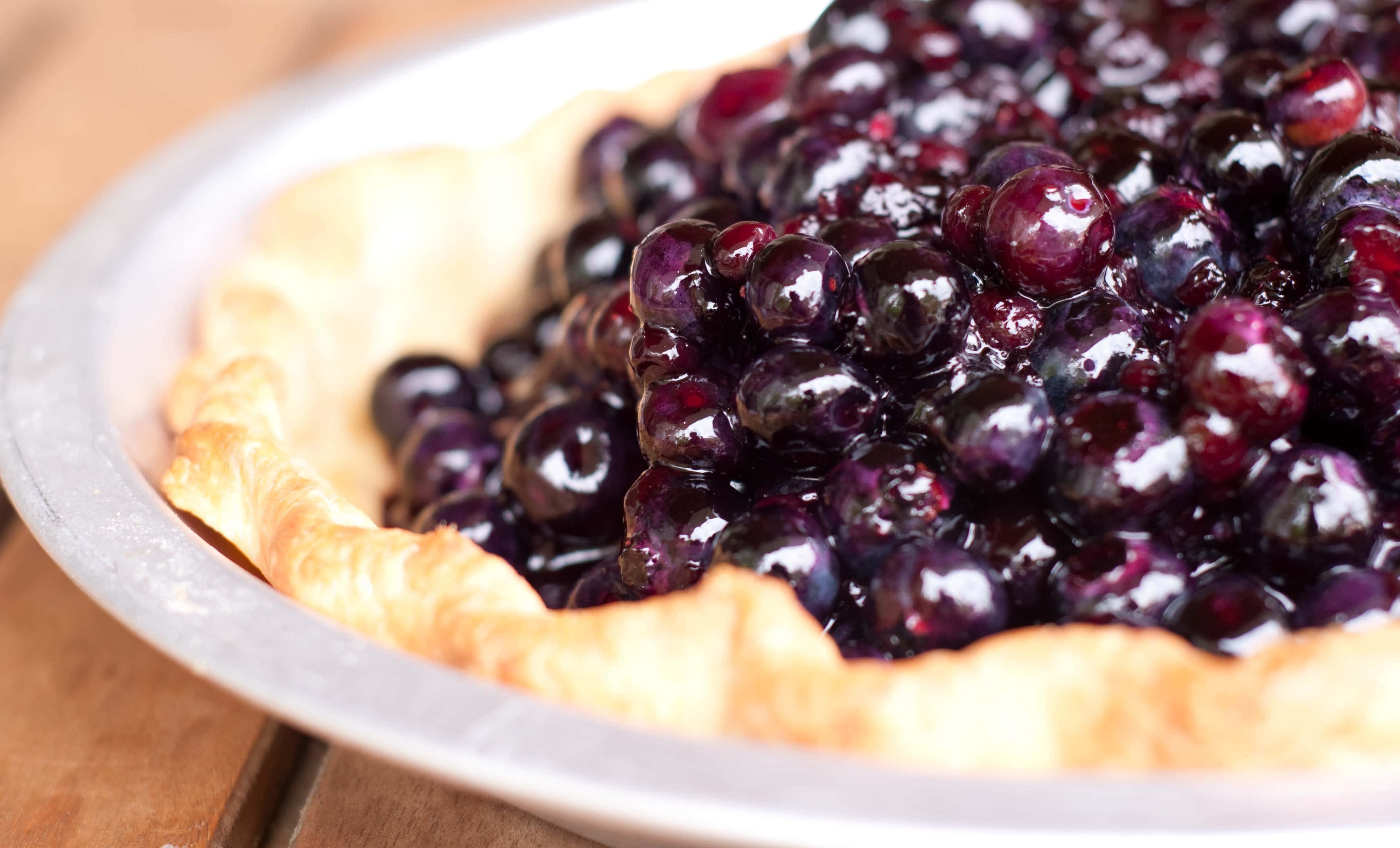 Blueberry Pie 桌布 壁紙 — 新鮮出爐藍莓批的特寫，閃亮的莓果從金屬盤中的金黃色外皮溢出。