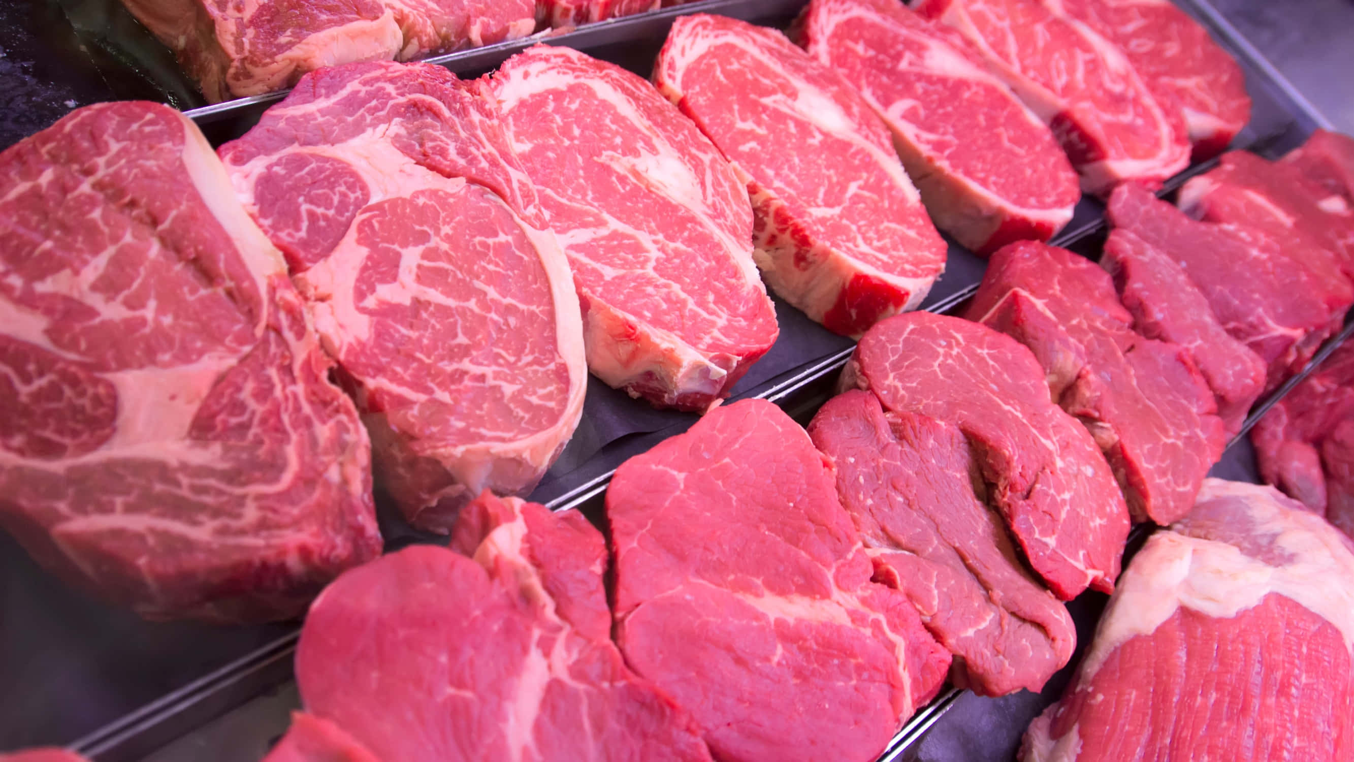 meat 桌布 壁紙 — 新鮮切割的頂級牛肉扒，帶有雪花紋理，展示在冷藏超市陳列櫃中。