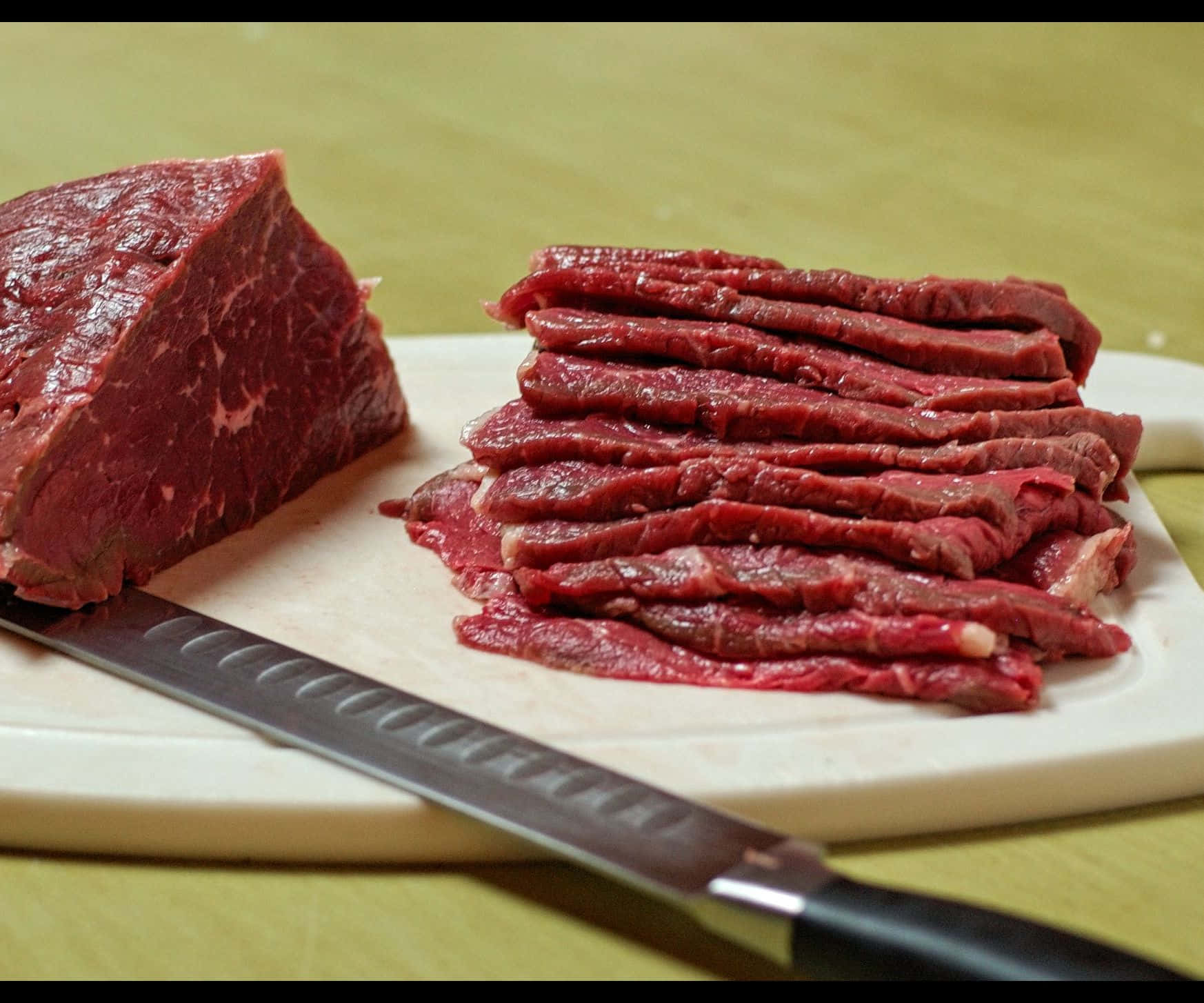 meat 桌布 壁紙 — 新鮮切好的生牛肉整齊地排列在白色砧板上，旁邊放著一把鋒利的刀。