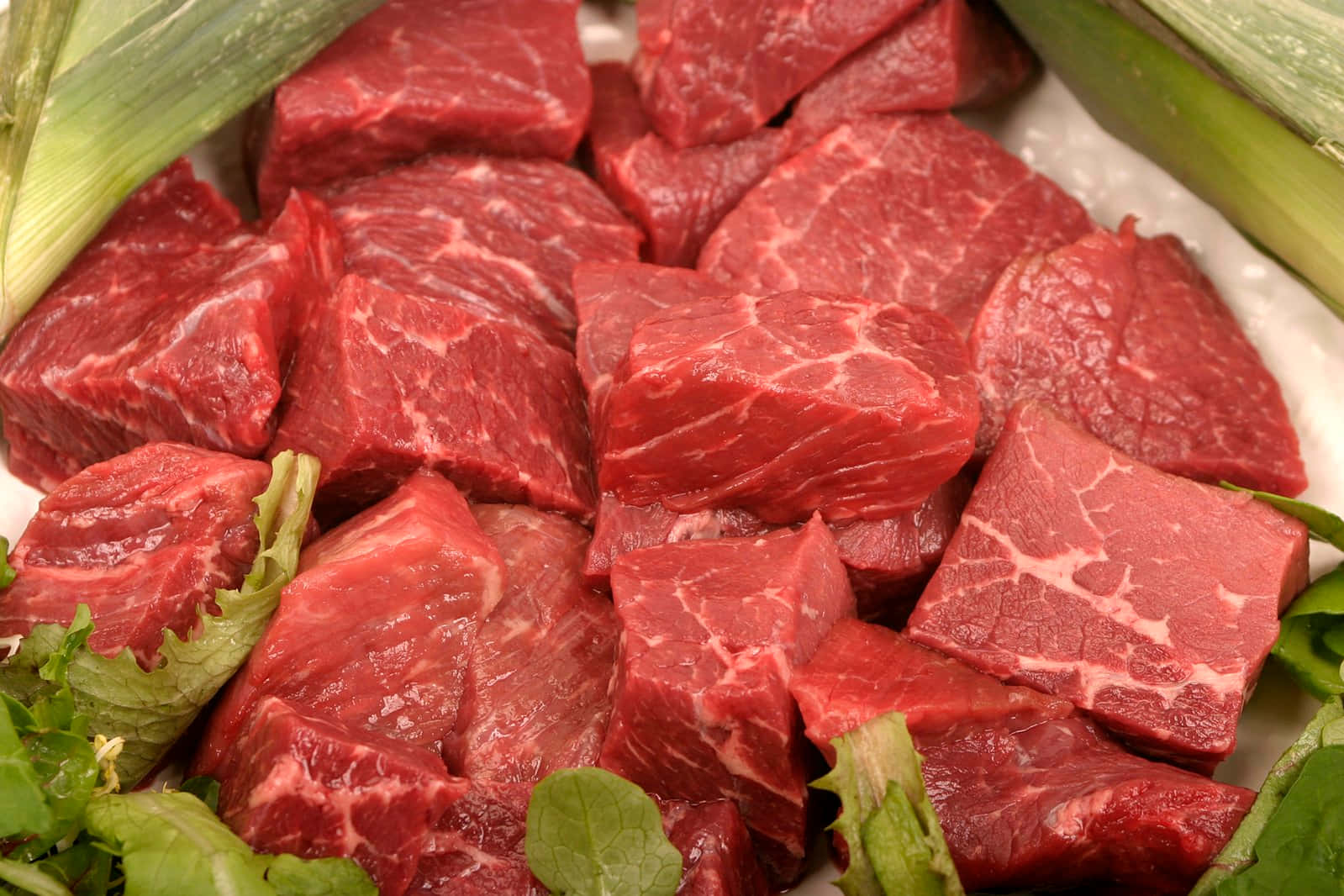 meat 桌布 壁紙 — 新鮮切好的紅色牛肉粒，帶有白色大理石紋，被綠色韭蔥和生菜圍繞，放在白色碟子上。