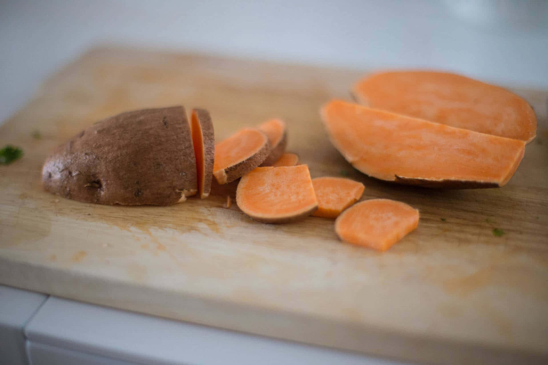 Yellow Sweet Potato 桌布 壁紙 — 新鮮切片嘅番薯，帶有鮮豔橙色嘅果肉，放喺木砧板上。