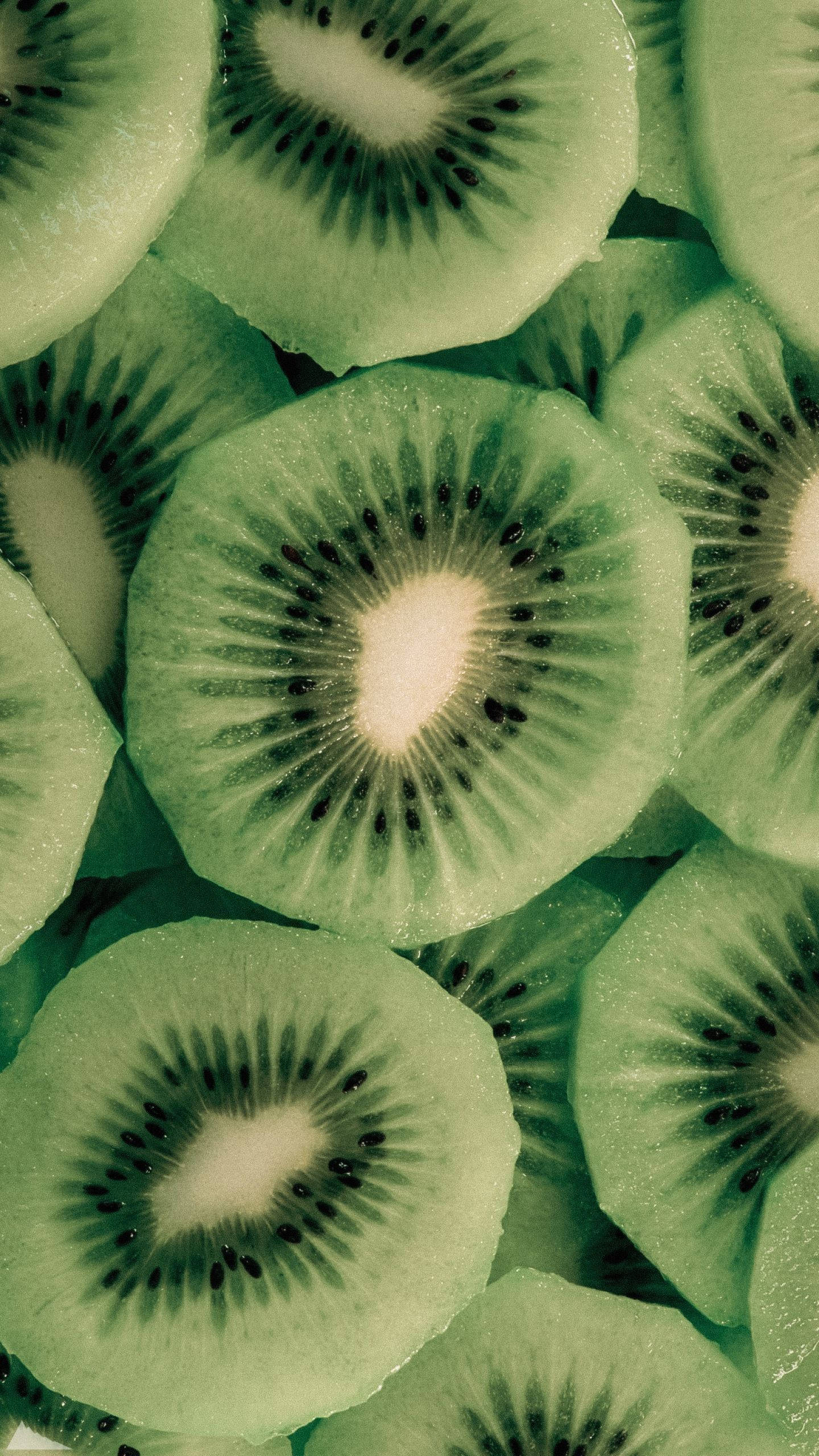 Kiwi 桌布 壁紙 — 新鮮切片奇異果的特寫，展現其鮮綠色果肉和黑色種子形成的密集圖案。