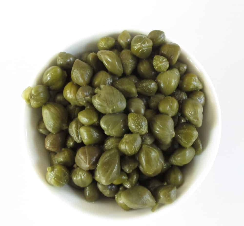 新鮮刺山柑花蕾盛於粗陶碗中 壁紙 — 從上方俯瞰，白色陶瓷碗中裝滿了光澤的綠色酸豆，背景是純白色。